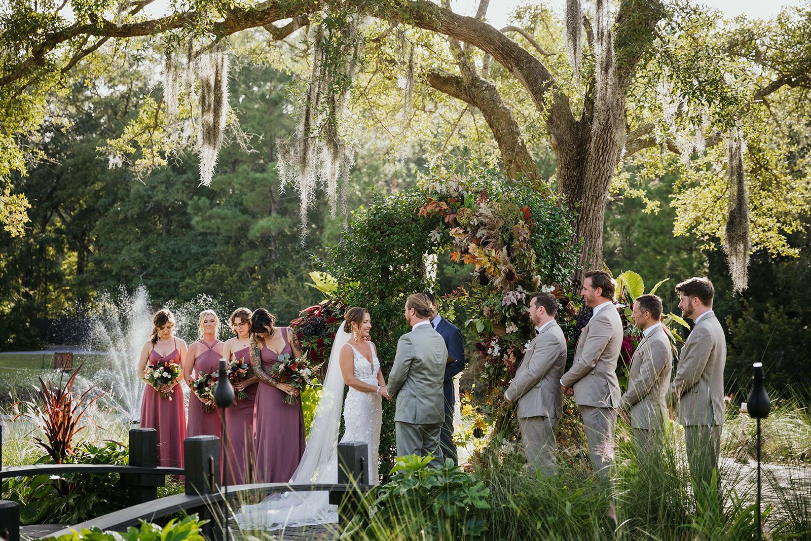 Wedding ceremony outdoors under a large tree, with the couple at the altar and attendants nearby.