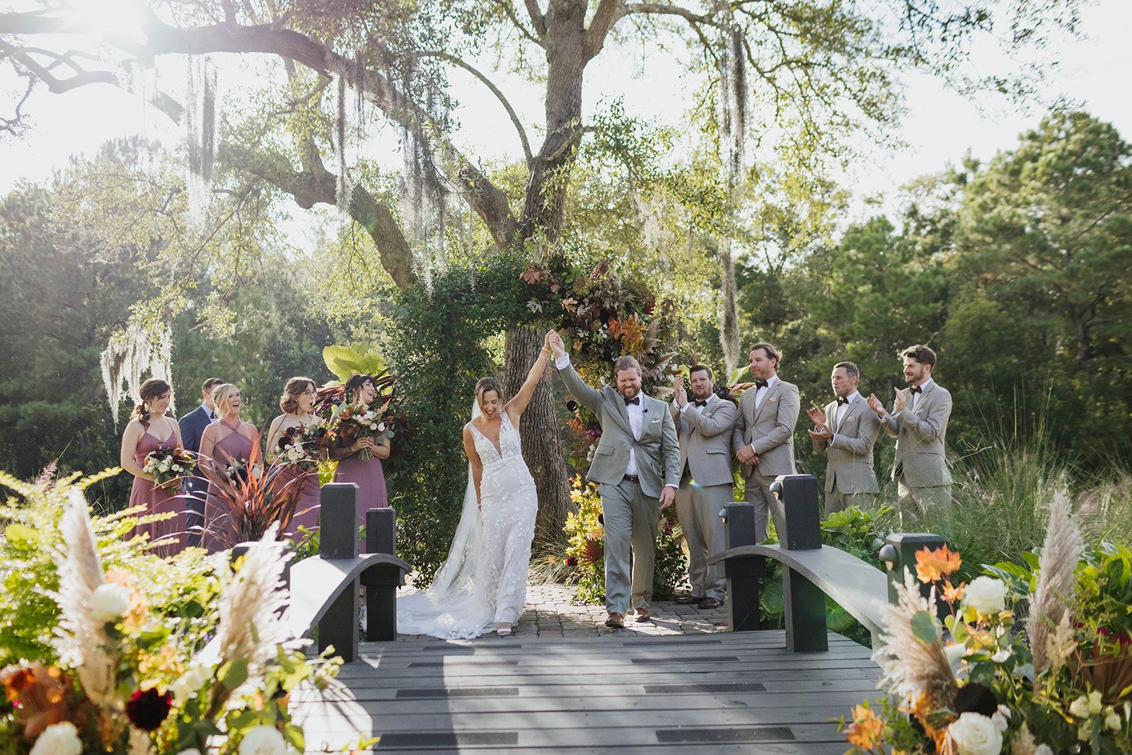 Outdoor wedding ceremony with bride, groom, and wedding party under sunlit trees
