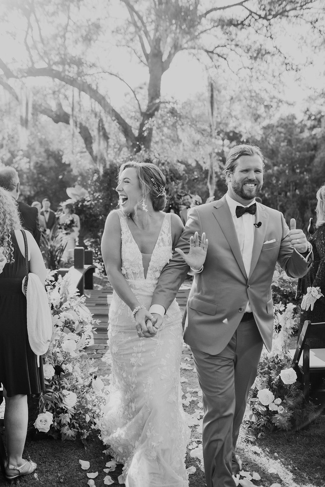 Bride and groom walking down an outdoor aisle, smiling amid floral decorations
