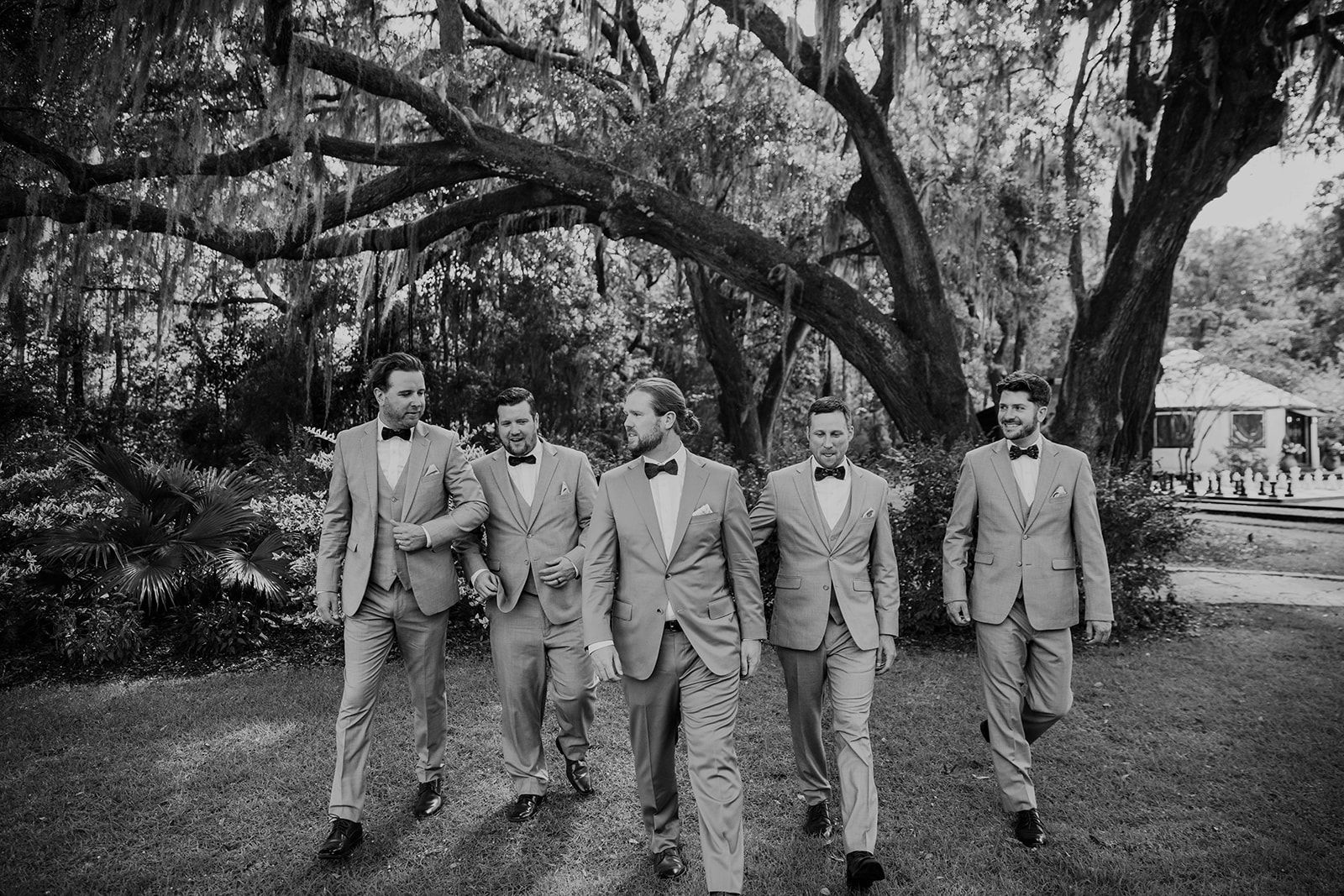 Five men in suits walking beneath a large tree in a park-like setting