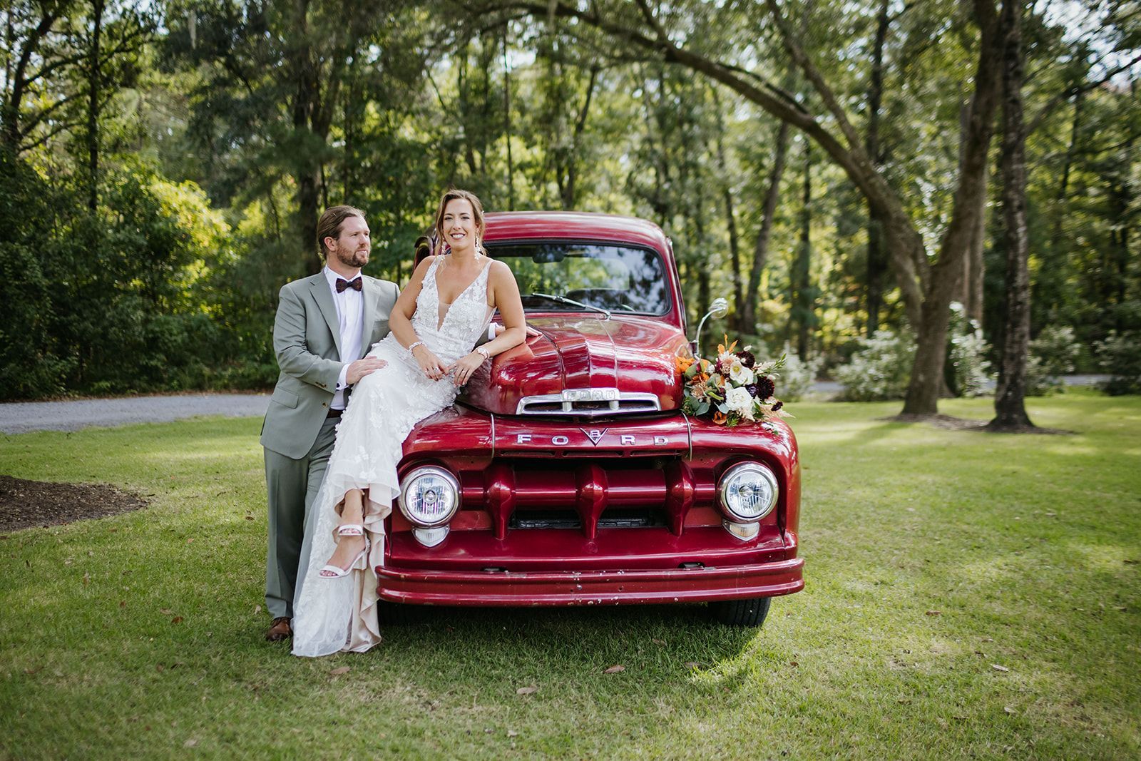 Bride and groom beside a red vintage truck in a grassy park