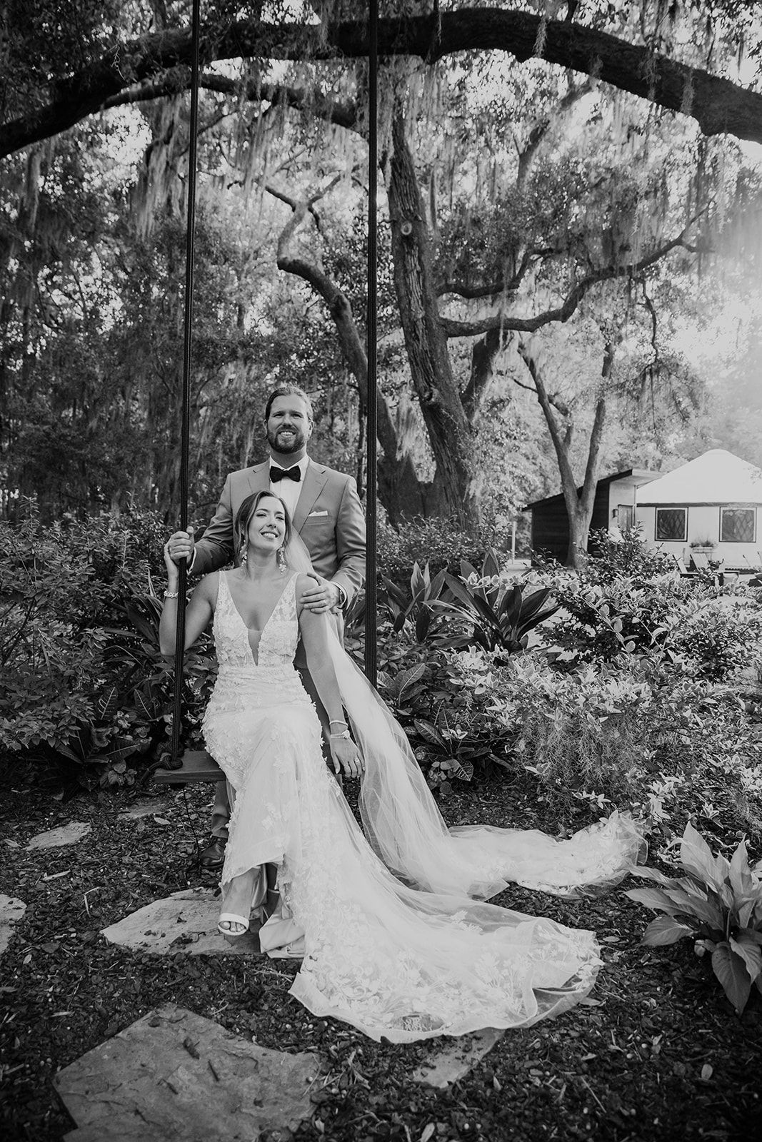 Bride and groom posing in a garden, with a long train and arching tree overhead