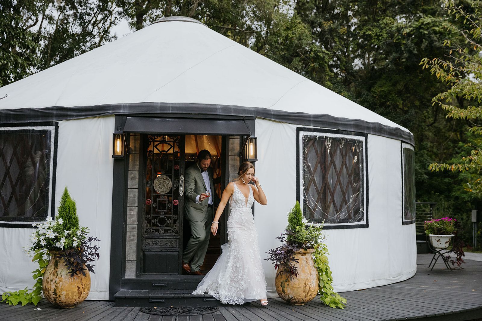 Bride and groom exiting a white round venue with potted plants at the entrance
