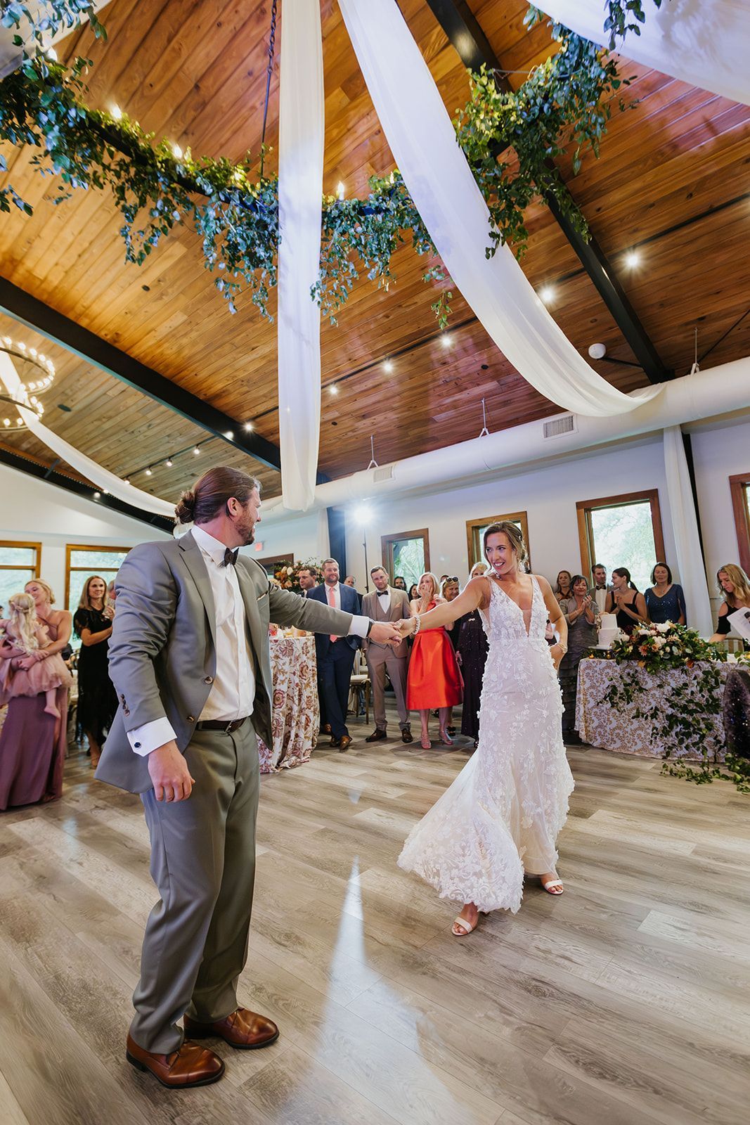 Bride and groom dancing in a decorated reception hall with draped white fabric and floral greenery.