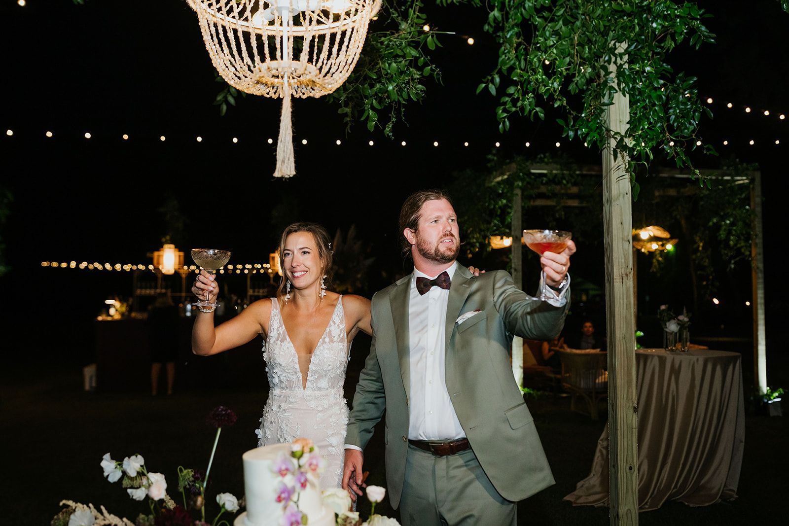 Bride and groom toasting under string lights at an outdoor wedding reception