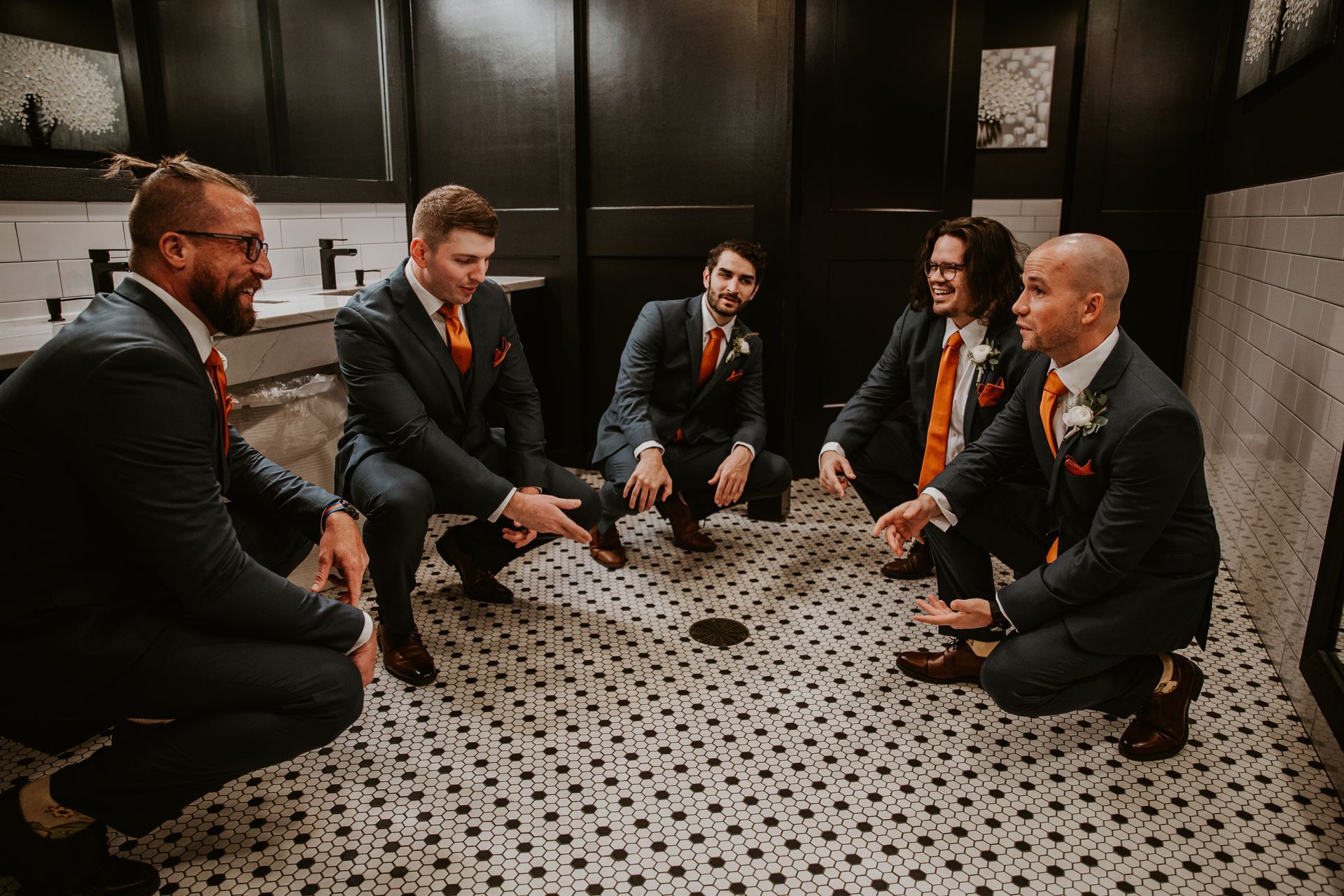 Five businesspeople in suits sit in a circle on a patterned floor, discussing in a dark room.