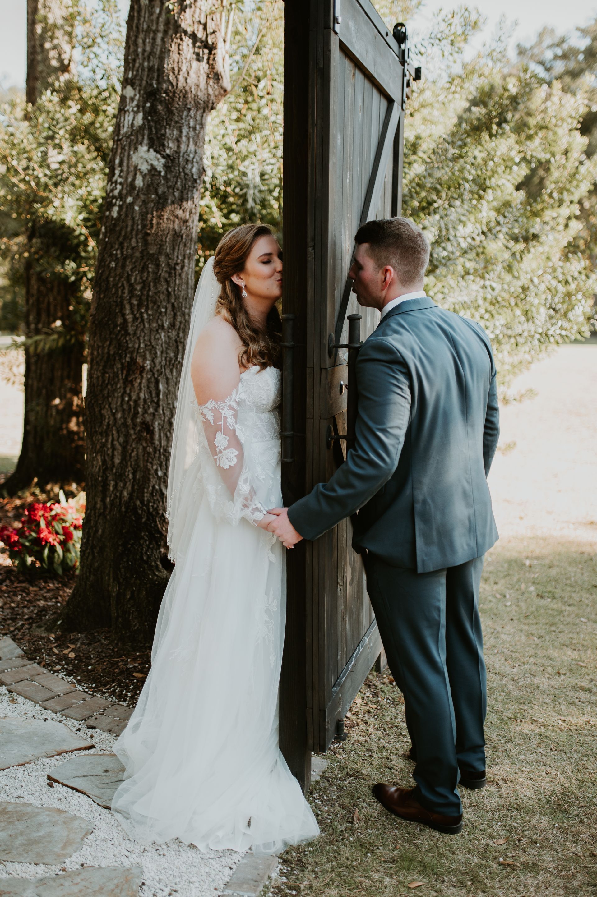 Bride and groom in wedding attire holding hands by a rustic barn door outdoors
