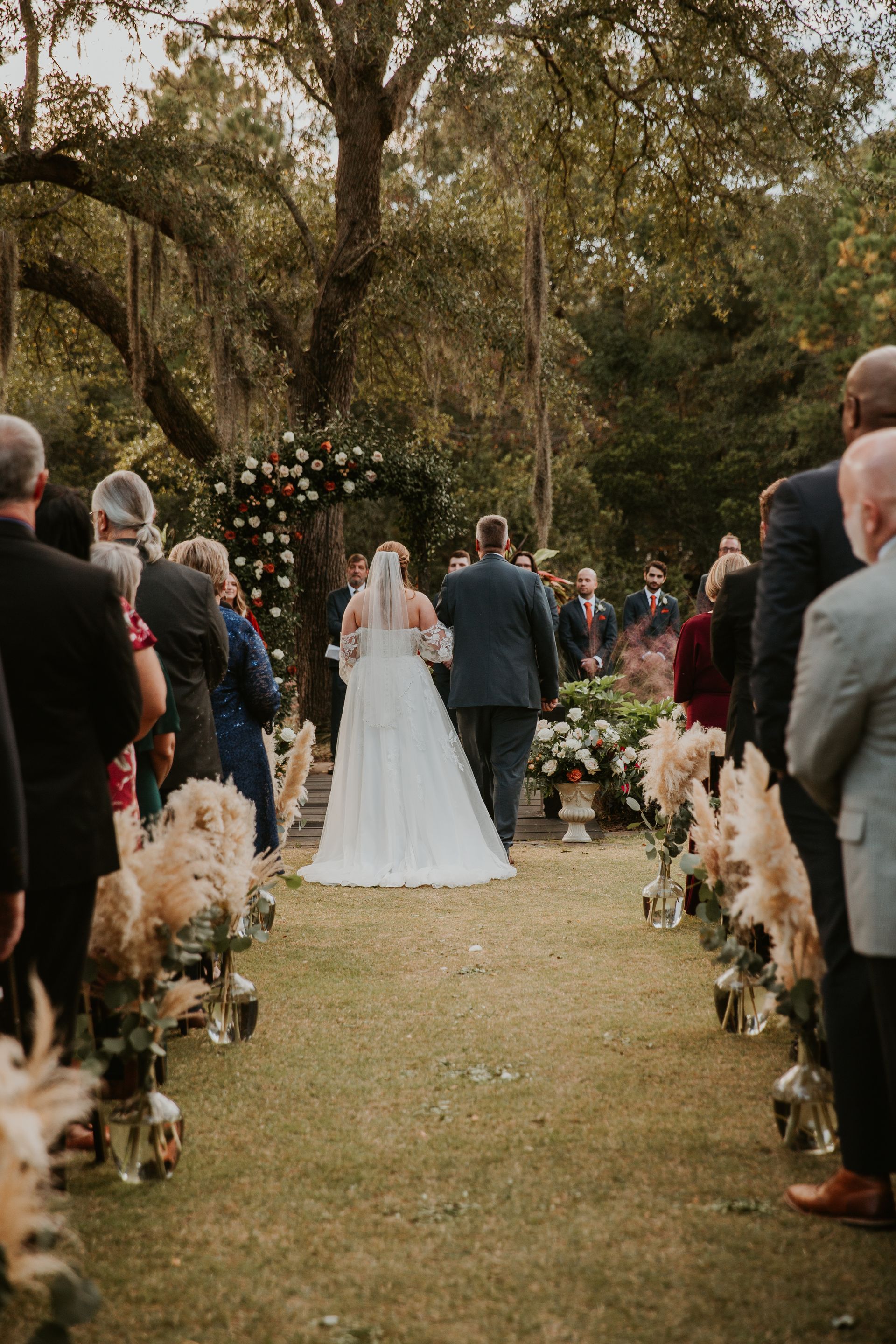 Bride and groom walking down a tree-lined aisle at an outdoor wedding ceremony