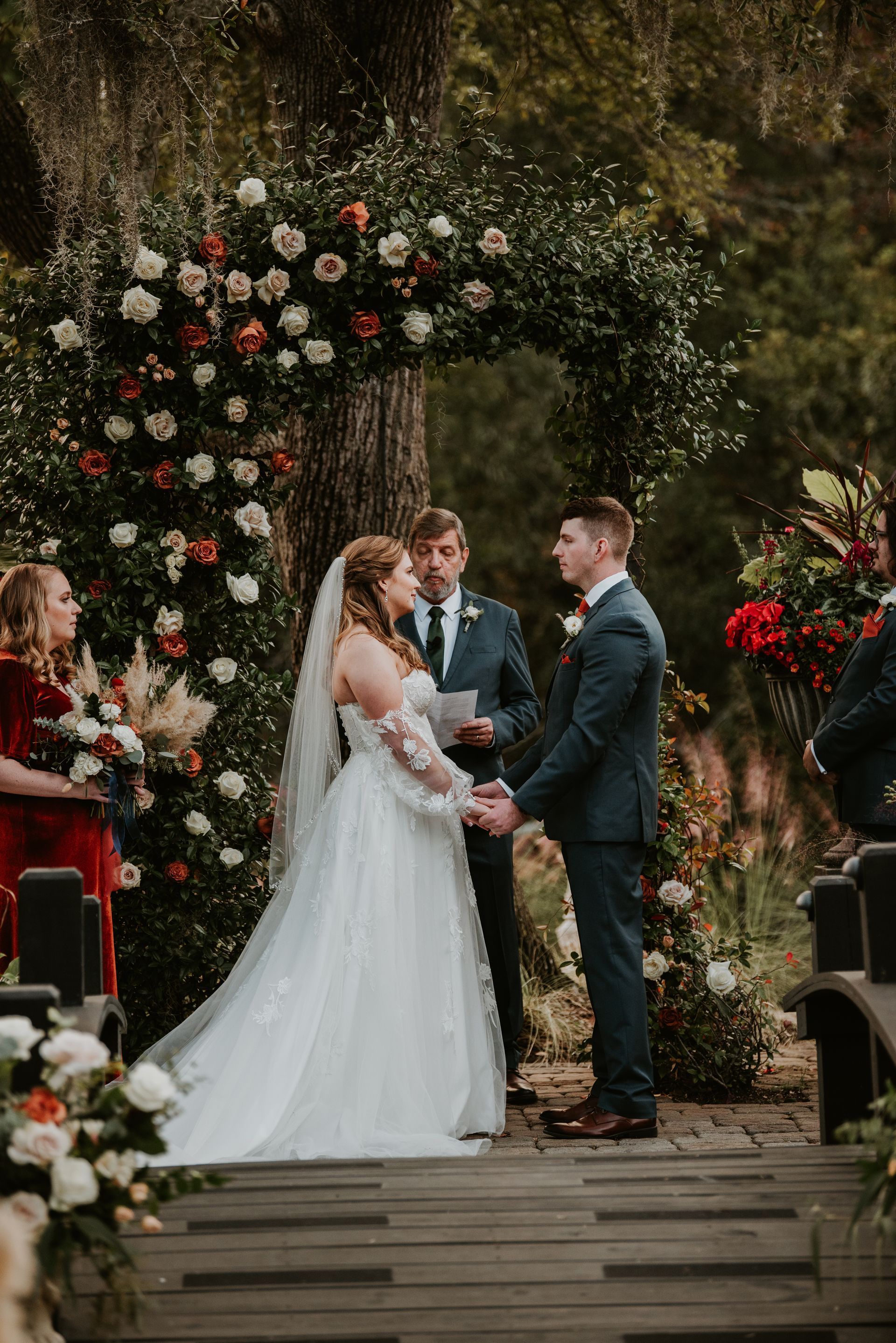 Wedding couple exchanging vows under floral arch at outdoor ceremony