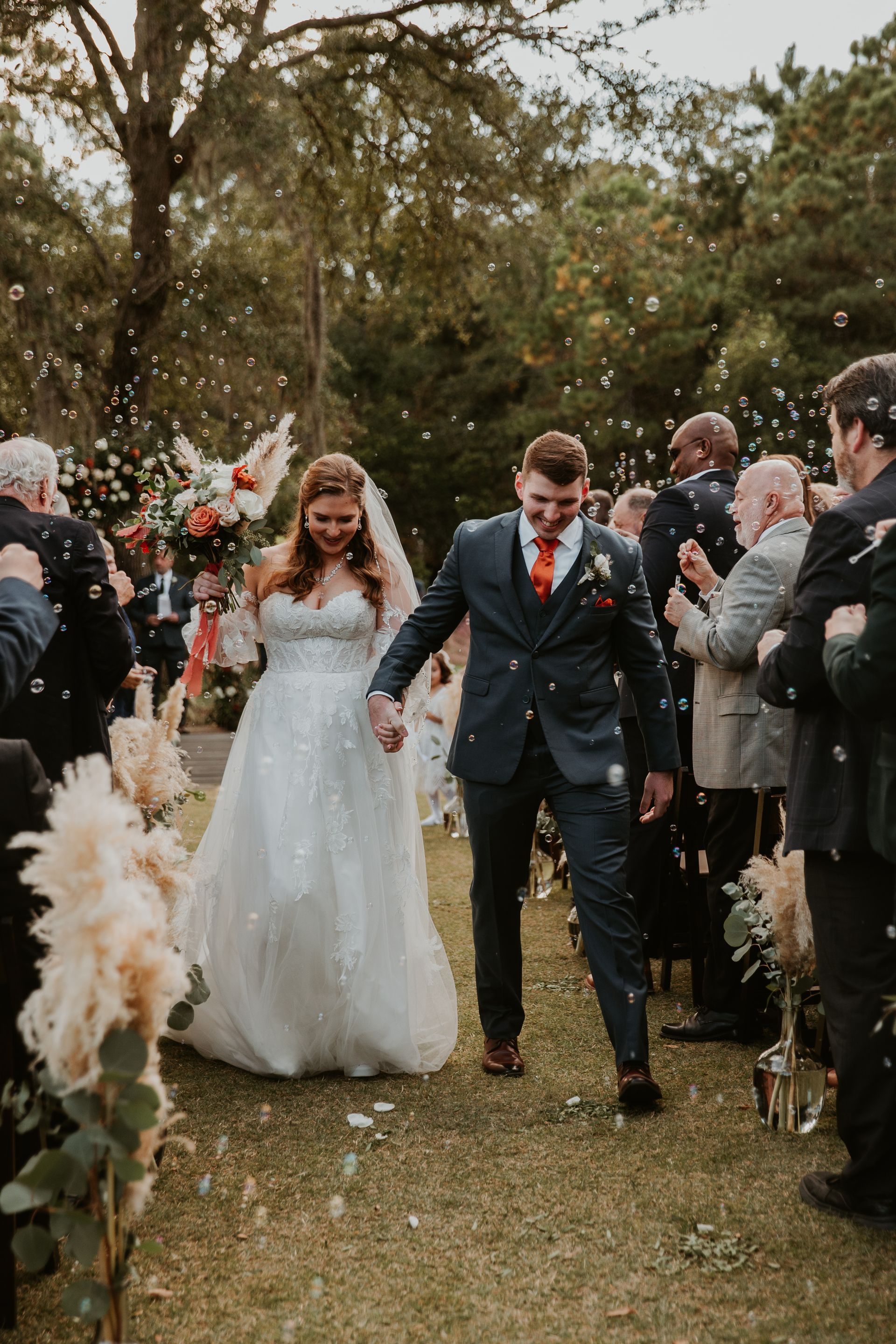 Bride and groom walking down a flower-lined outdoor aisle at a wedding ceremony