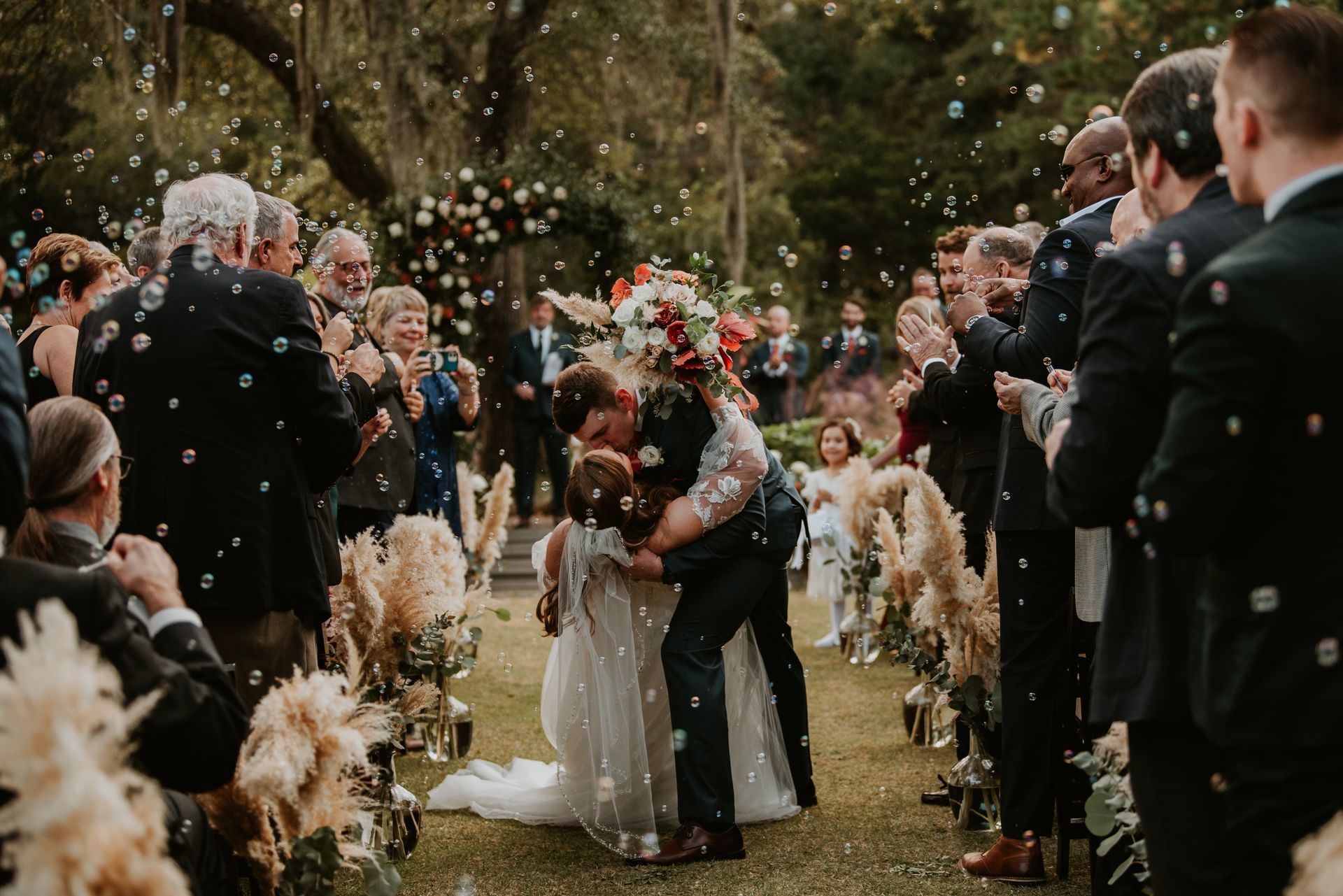 Wedding couple kissing outdoors as guests toss confetti and raise bouquets around them