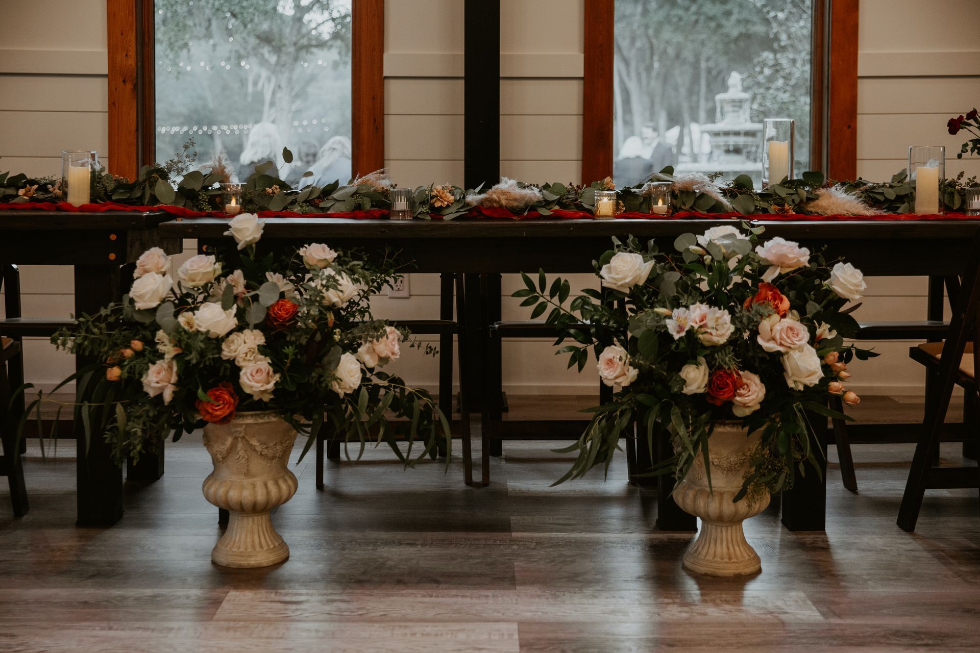 Elegant floral arrangements in cream, pink, and white on gold pedestals in front of a table by a window