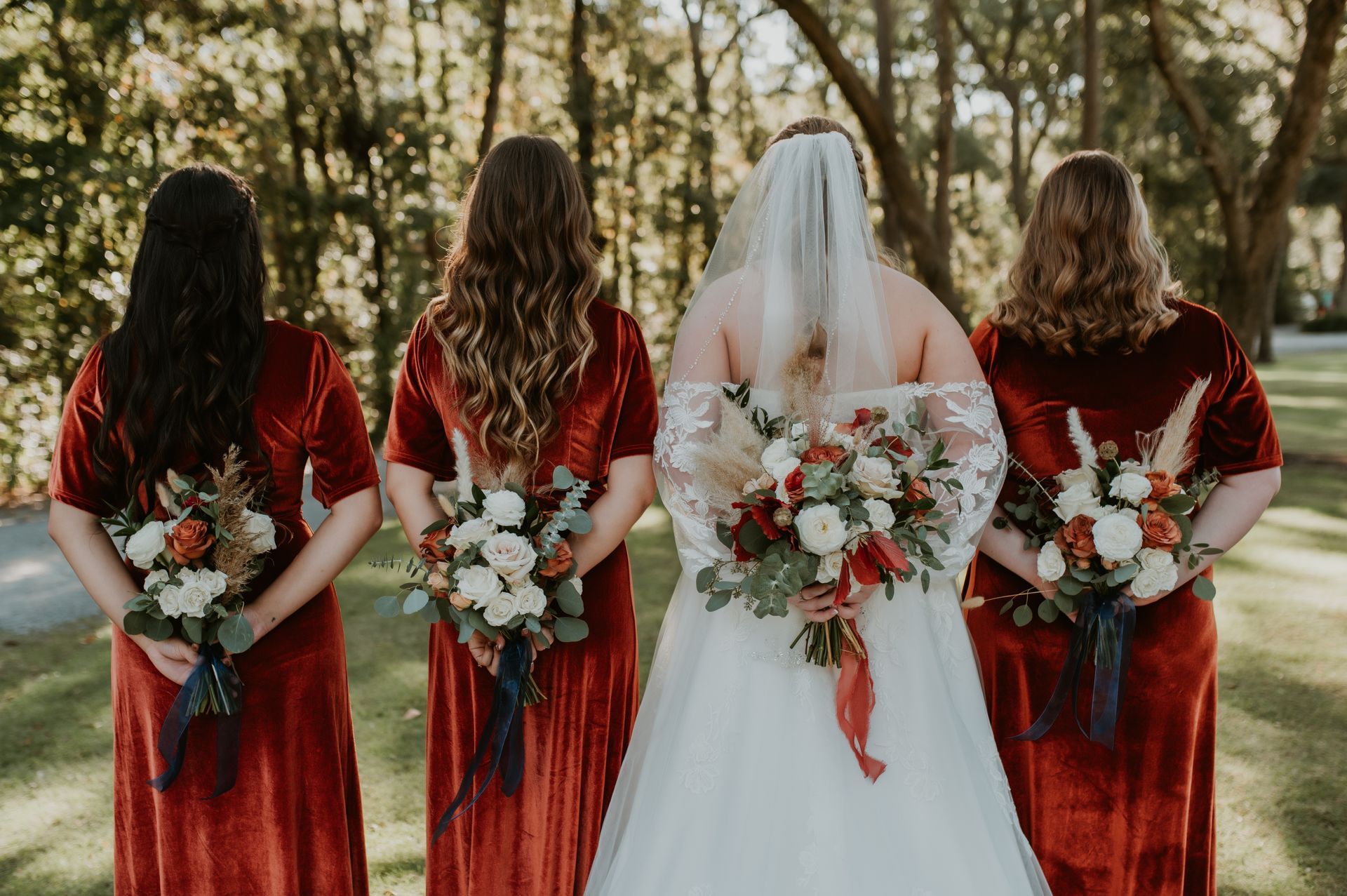 Bride and three bridesmaids in red dresses holding bouquets outdoors