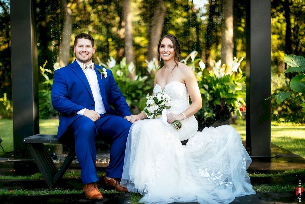Bride and groom seated outdoors in a garden, smiling in wedding attire