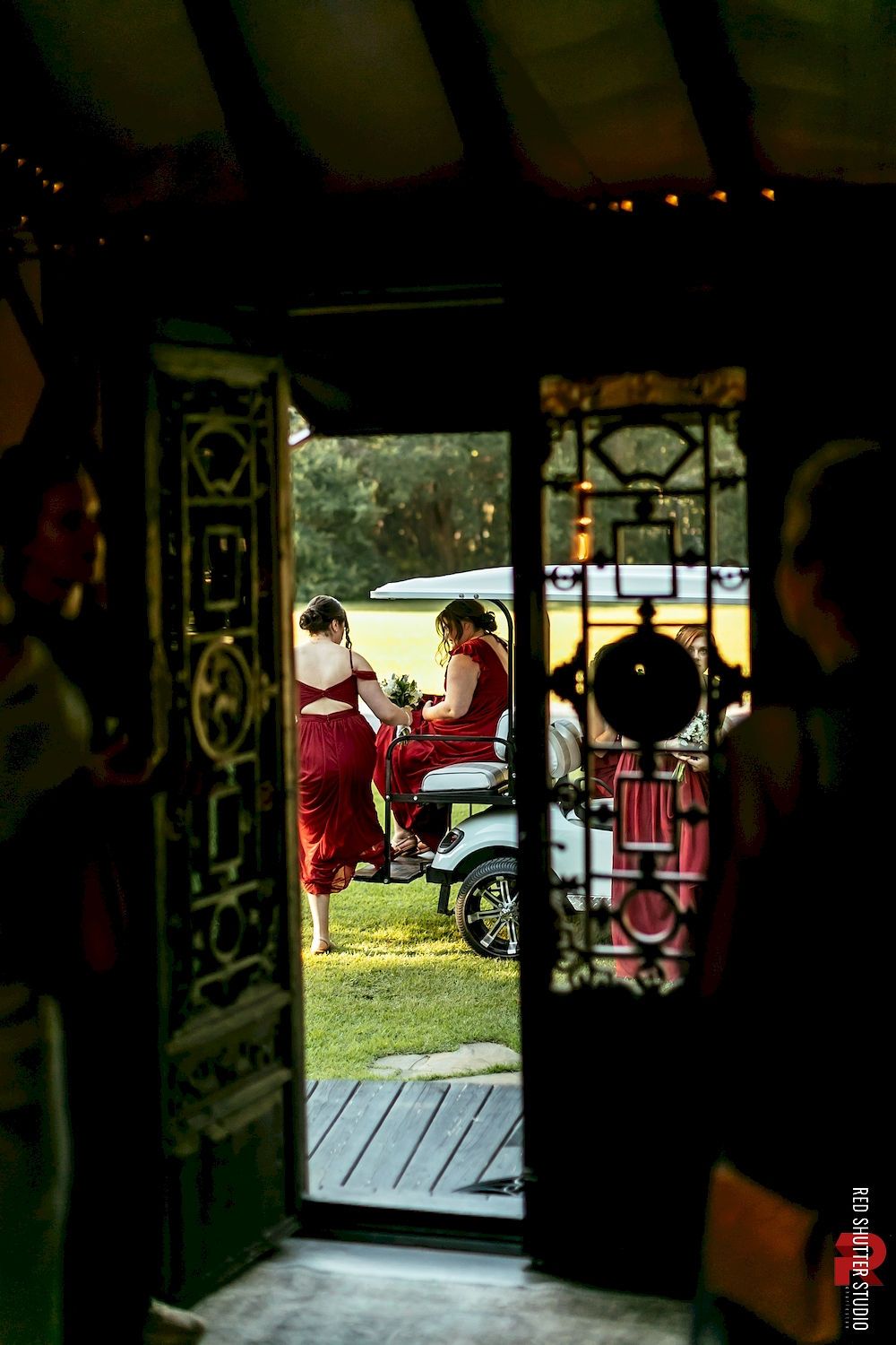 Open doorway framing people gathered outside beside a red motorcycle on a grassy area.