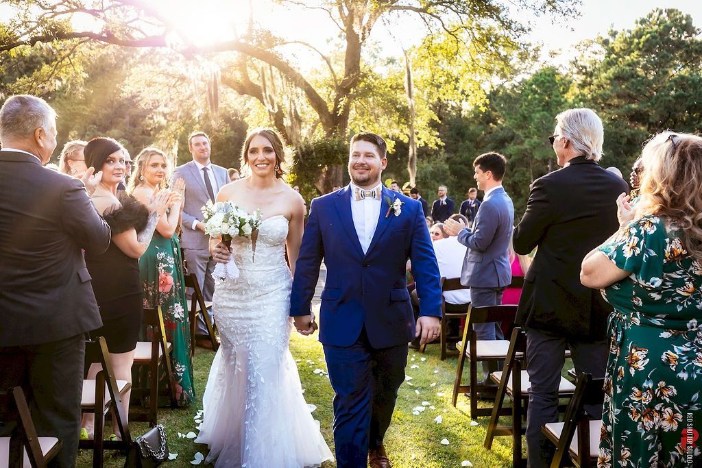 Bride and groom walking down an outdoor aisle, guests standing and applauding on both sides