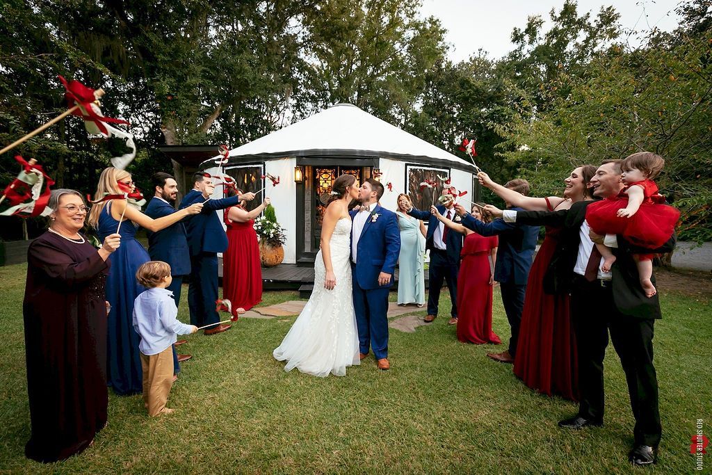 Bride and groom walk through guests cheering with raised arms in a garden wedding ceremony.