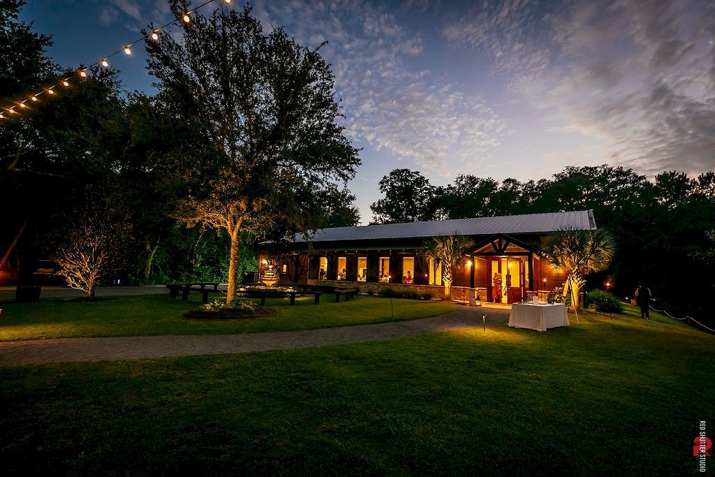 Lit house surrounded by trees and lawn at dusk, with warm lights glowing from the windows and patio.