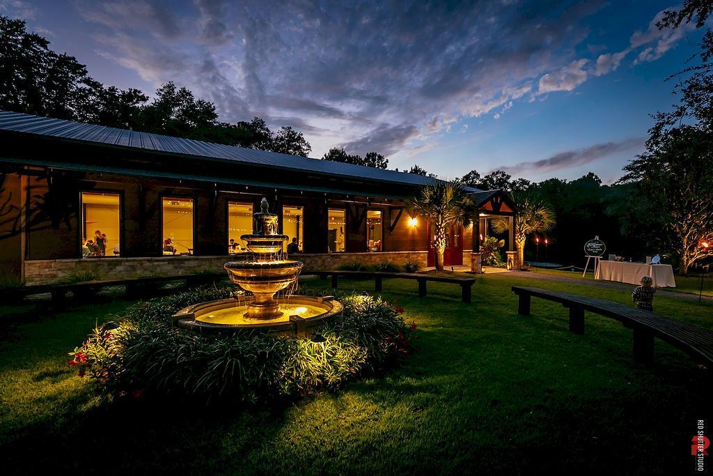 Nighttime garden courtyard with lit fountain and a long building under a dusky sky