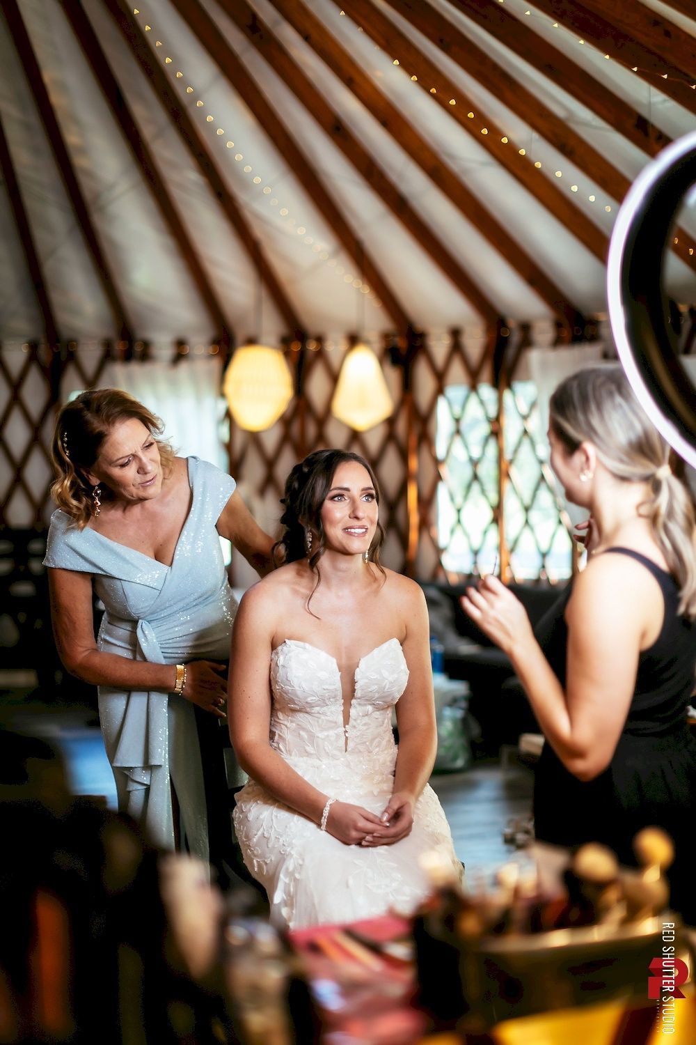 Bride getting ready in a yurt, with two women adjusting her dress and hair.