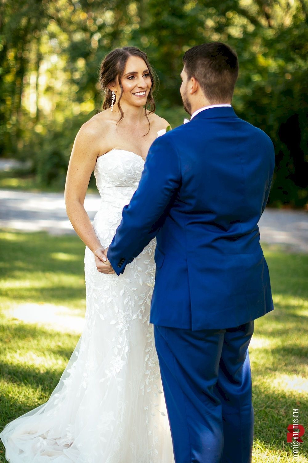Bride and groom holding hands outdoors in a sunlit garden, facing each other during their wedding ceremony