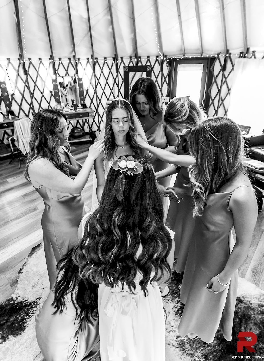 Group of people standing in a circle, reaching toward a central person indoors with curtains in the background