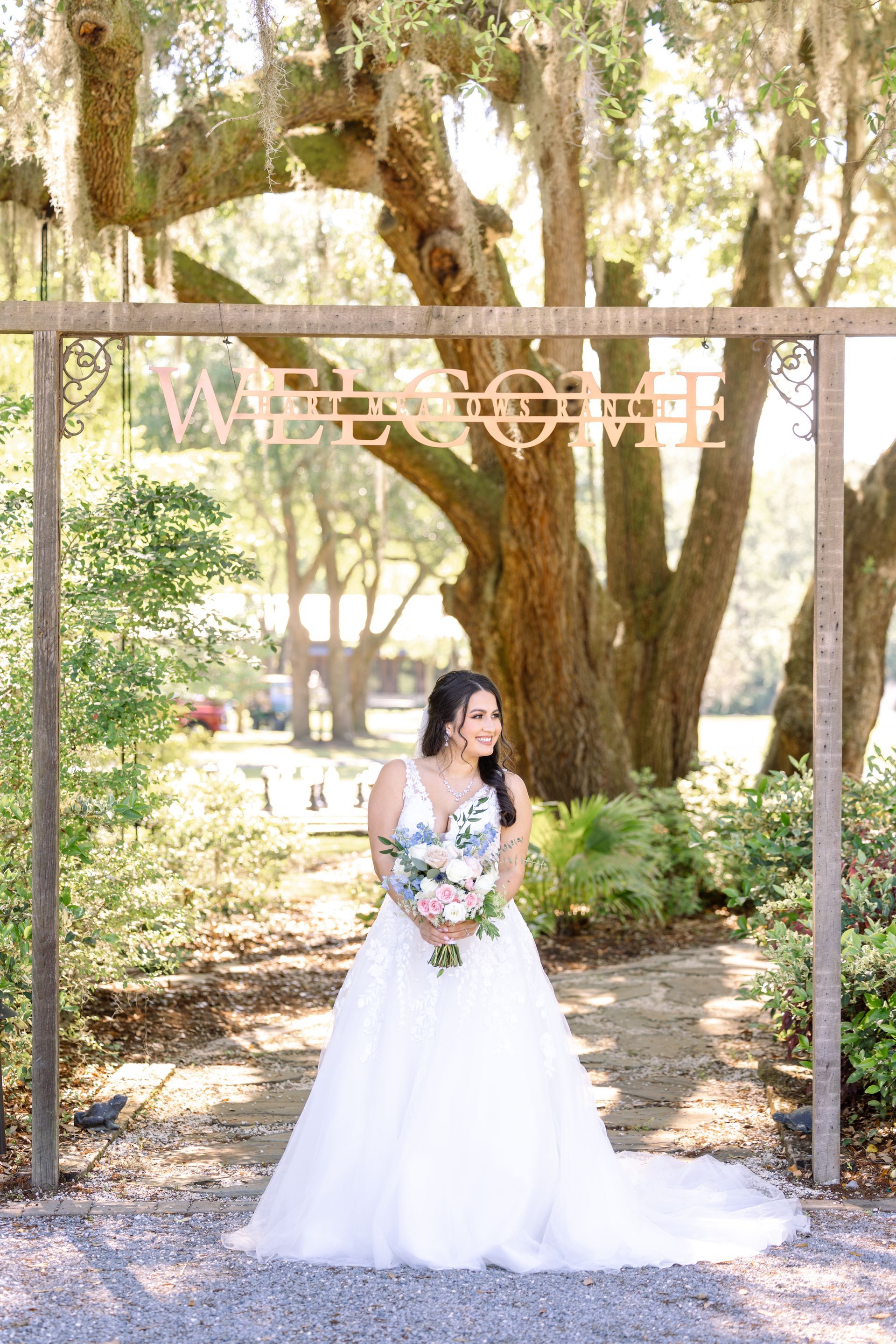 Bride in a white gown holding a bouquet under a wooden arch in a garden