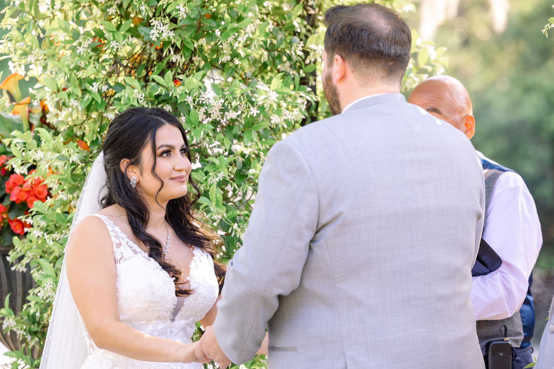 Bride and groom speaking outdoors at a wedding, with floral greenery in the background
