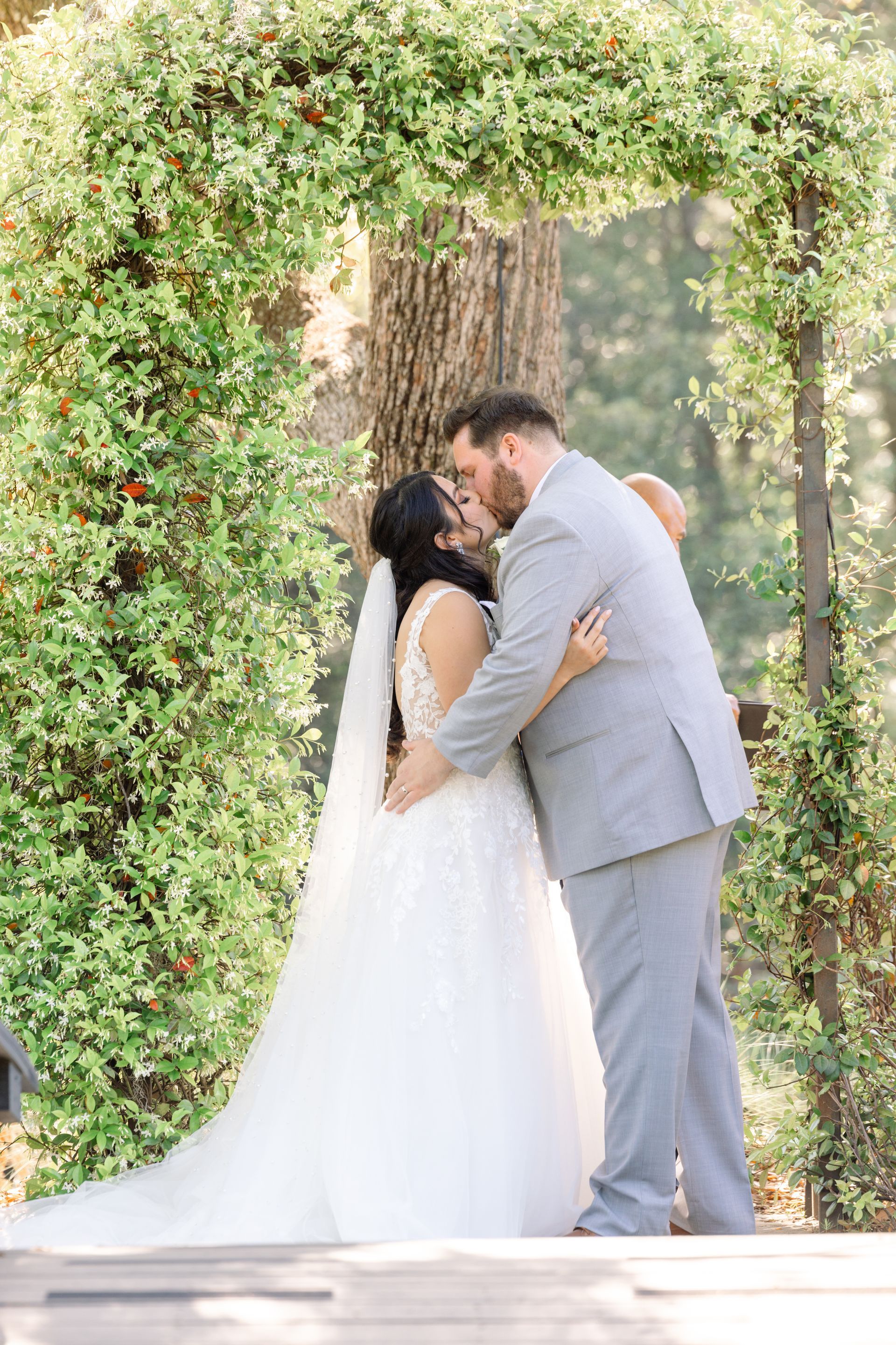 Bride and groom kissing under a leafy wedding arch outdoors