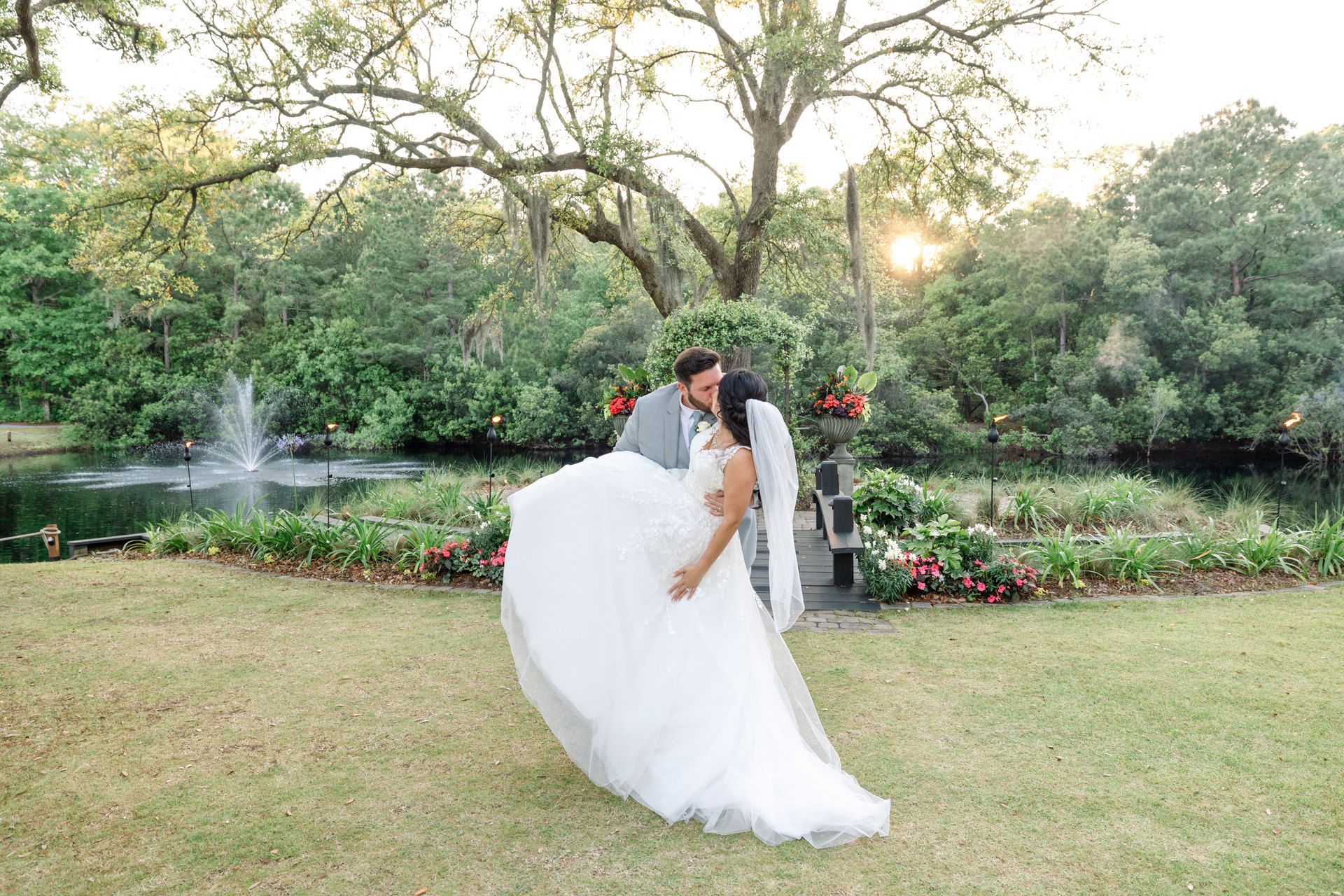 Bride and groom kissing in a garden, with a fountain and trees in the background