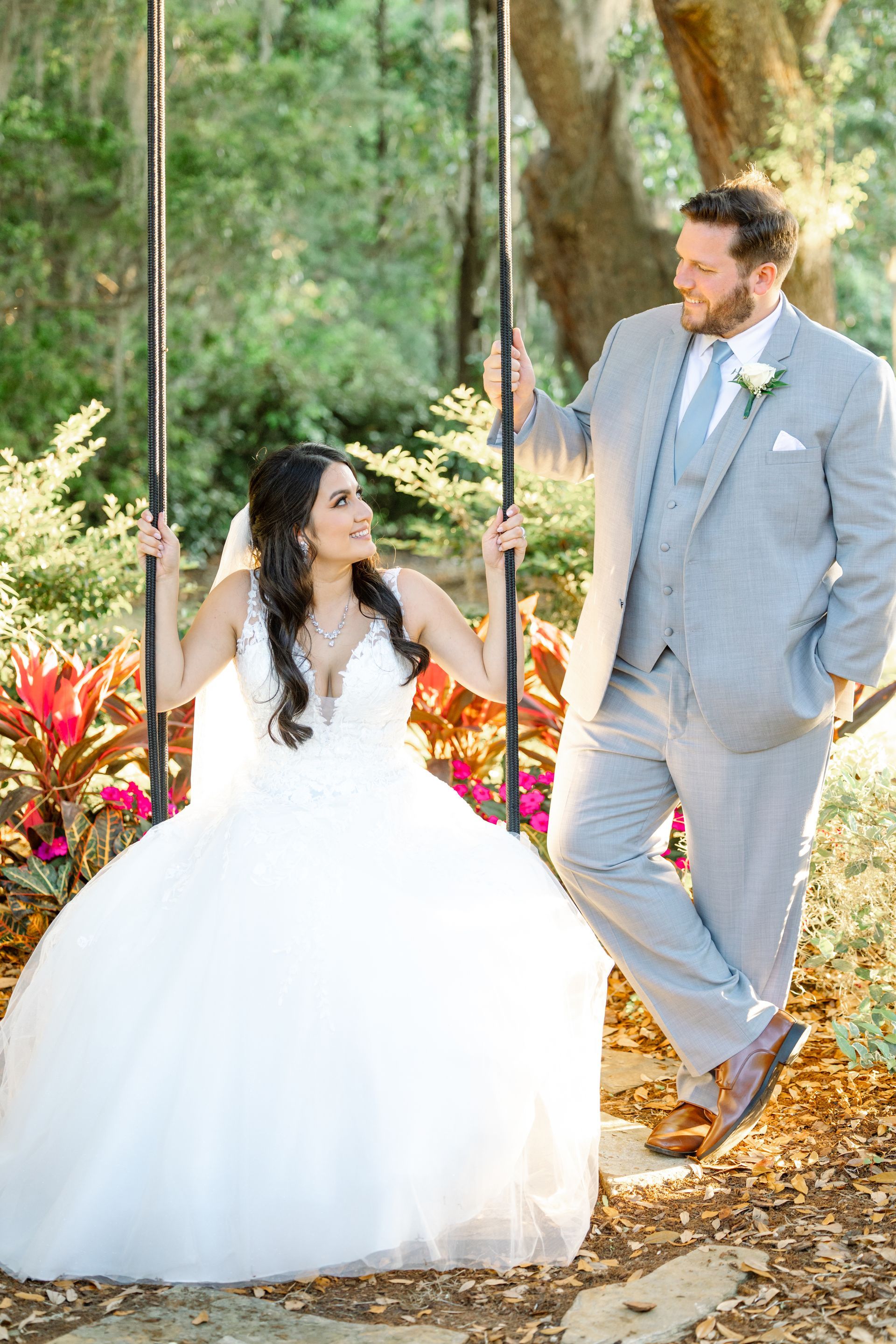 Bride in a white gown and groom in a gray suit standing together in a wooded outdoor setting