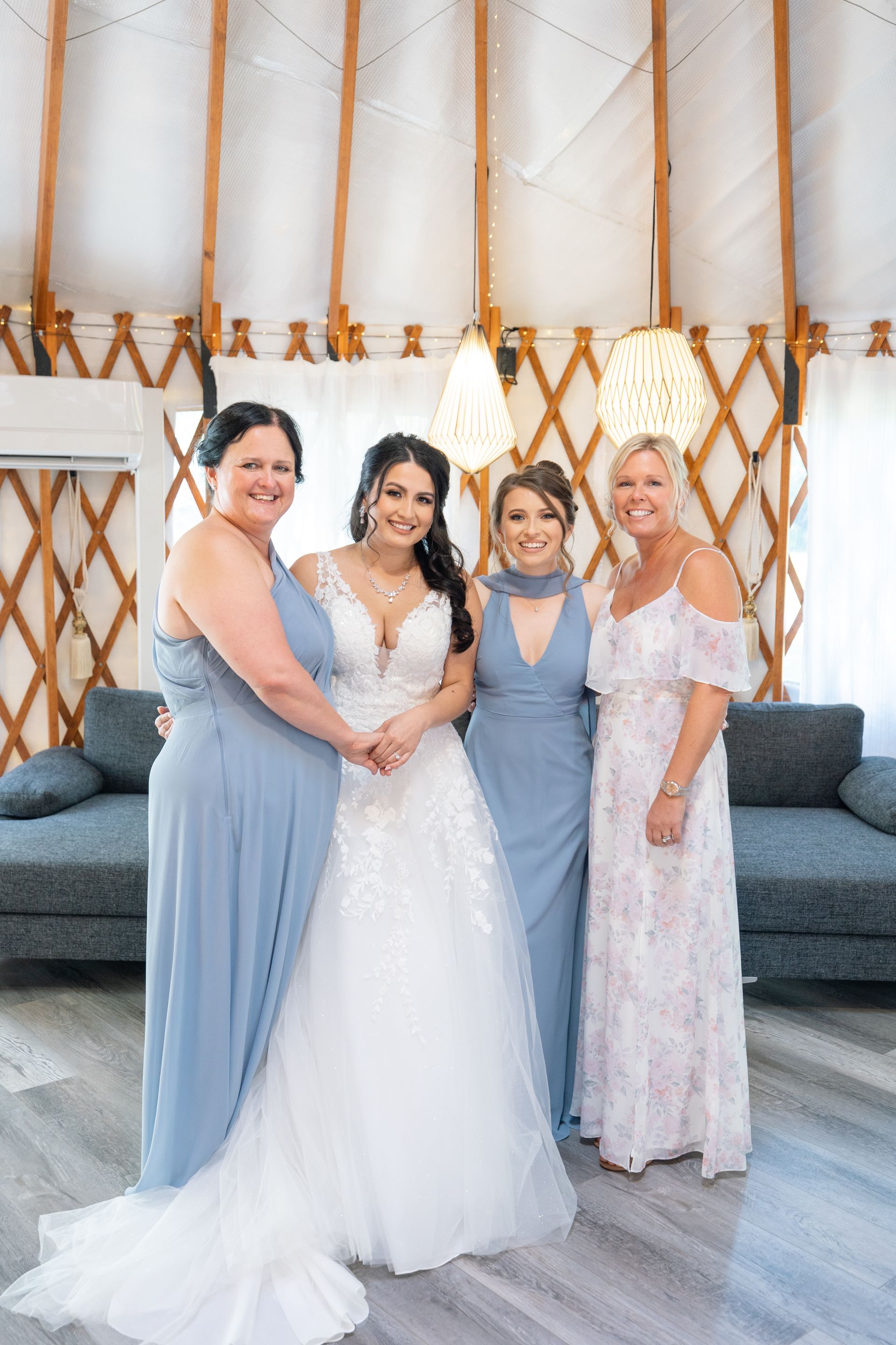 Four people posing in formal dresses in front of a wooden yurt-style backdrop