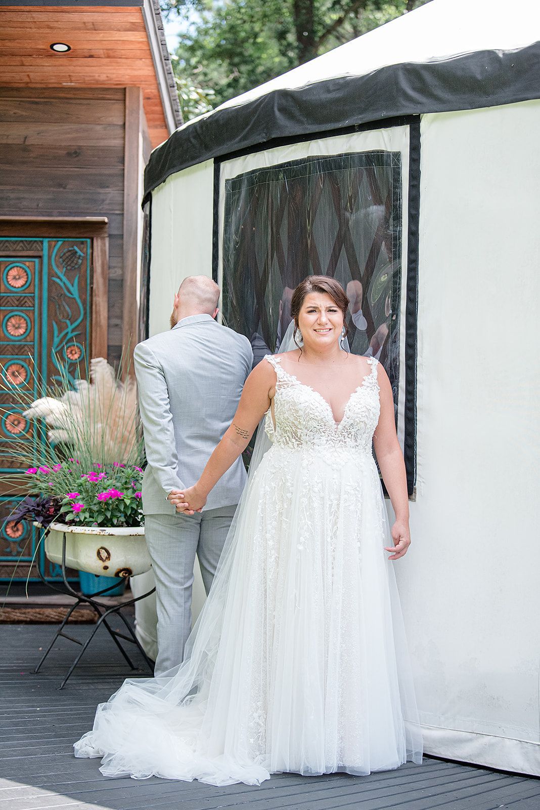 Bride in a white lace gown standing outdoors beside a tented venue.