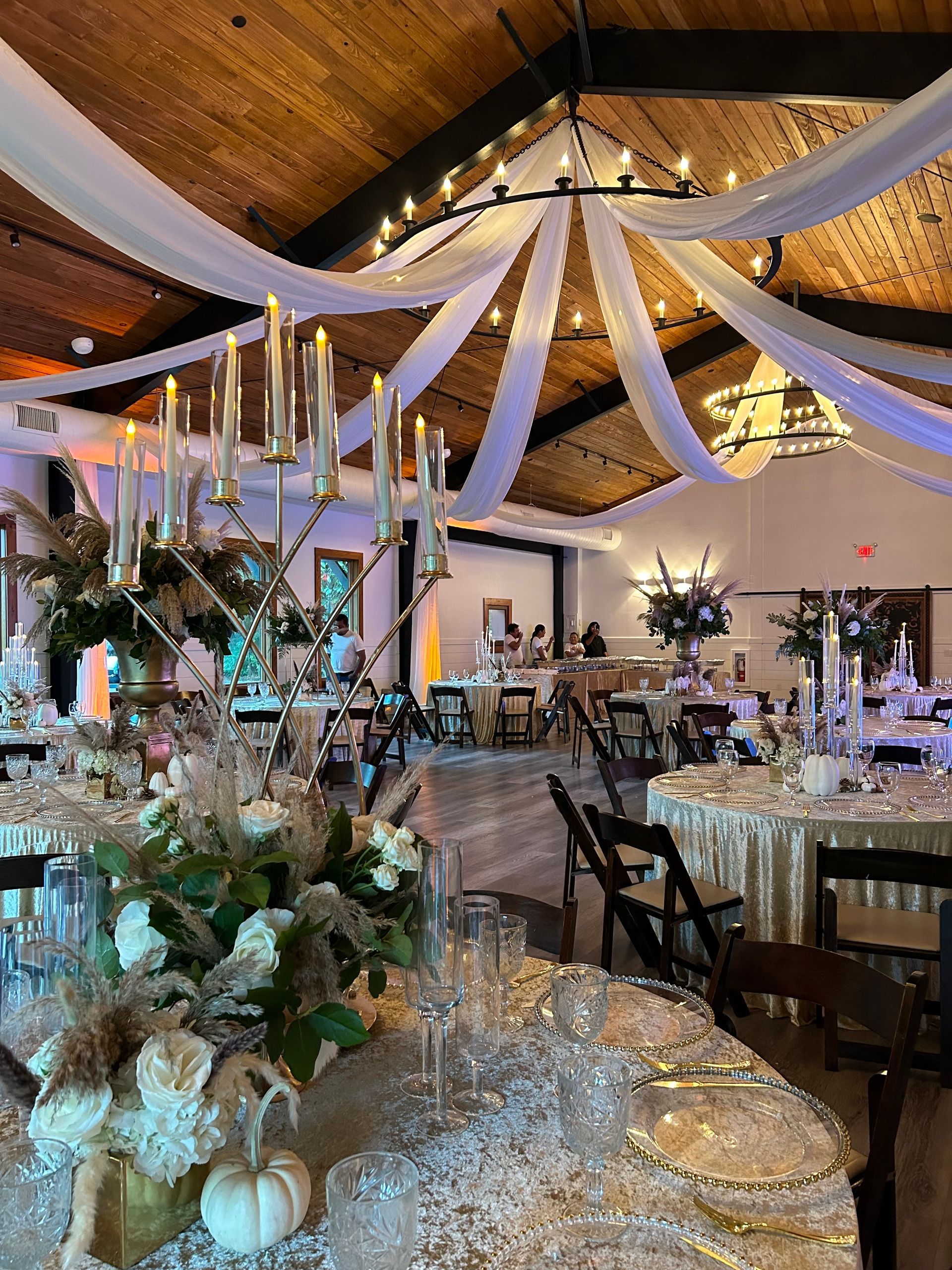 Elegant wedding reception hall with draped white fabric, warm lights, and floral table centerpieces.