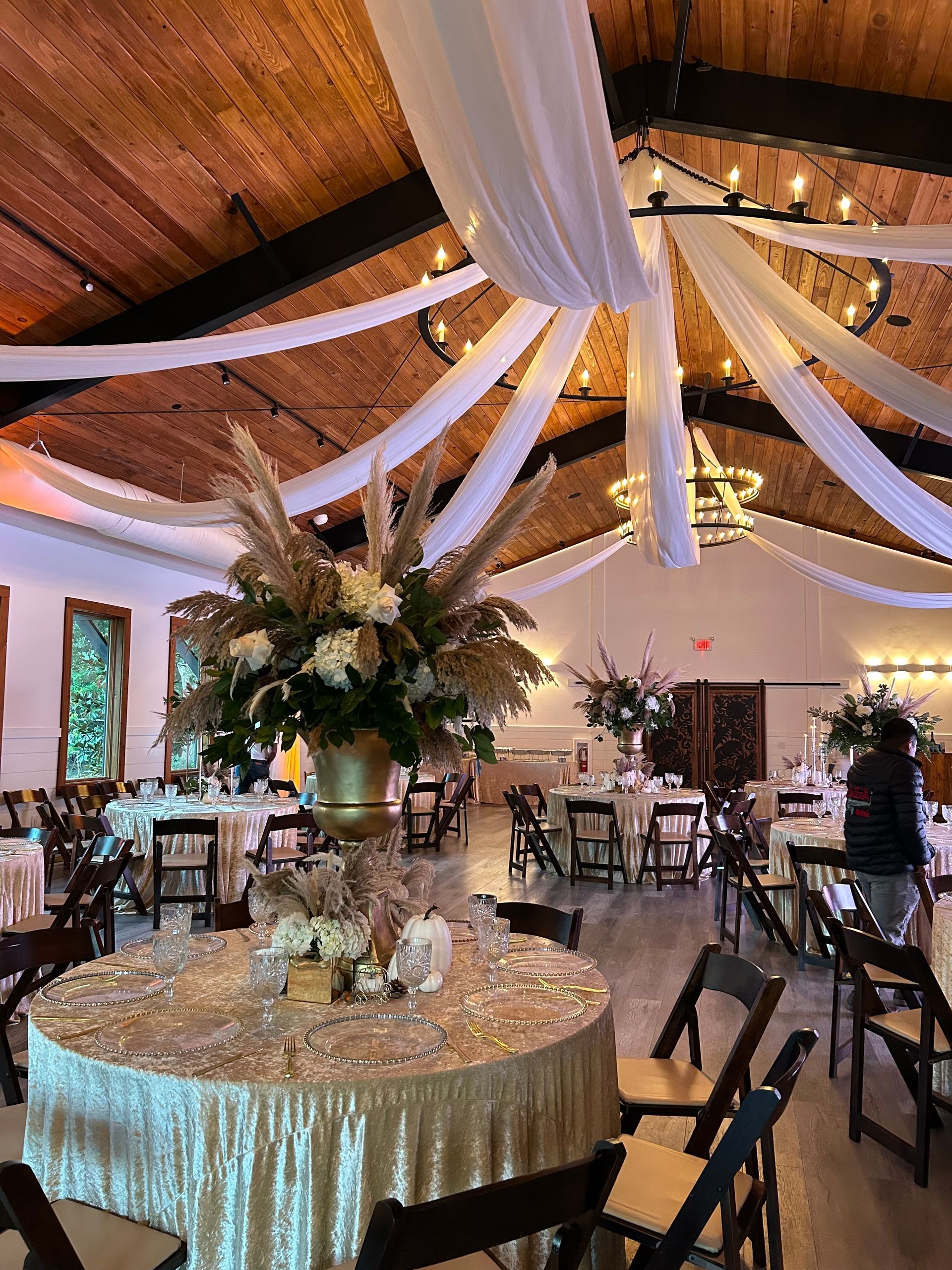 Elegant banquet hall with draped white fabric, floral centerpieces, and round tables set for an event