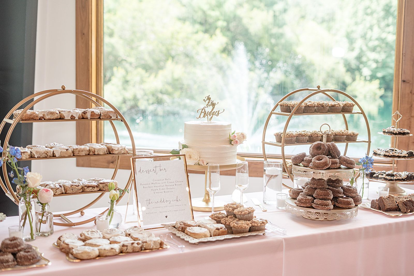 Elegant dessert table with tiered cakes, pastries, and gold serving stands by a bright window