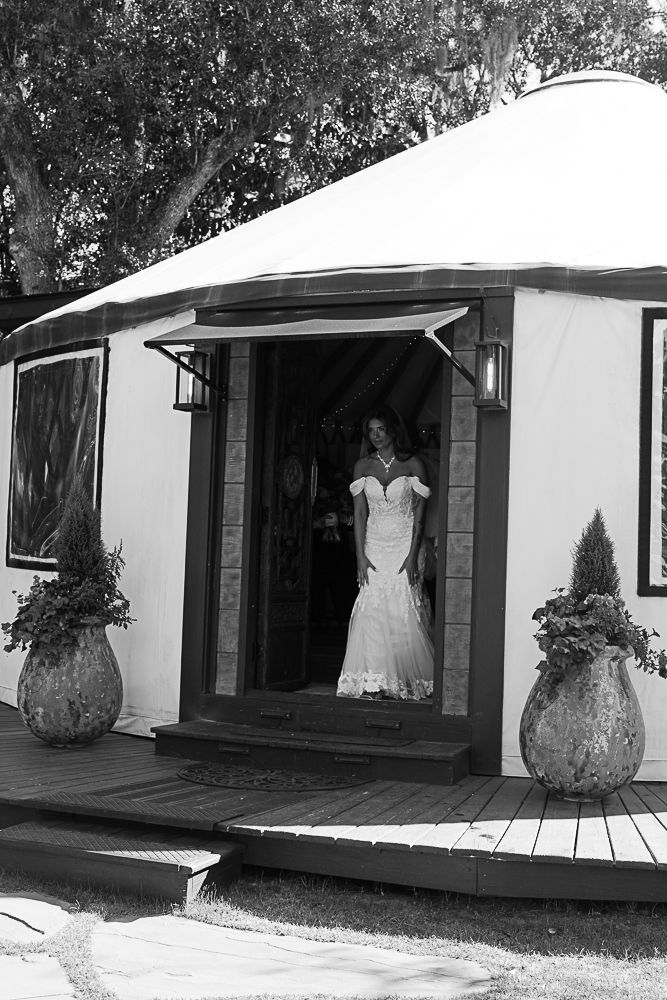 White-walled cottage entrance with a woman in a gown standing in the doorway, flanked by potted plants