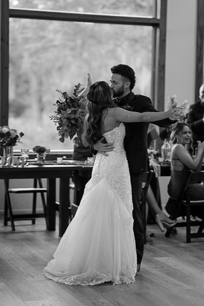 Couple slow dancing at a wedding reception in a bright hall, bride in a white gown and groom in a dark suit