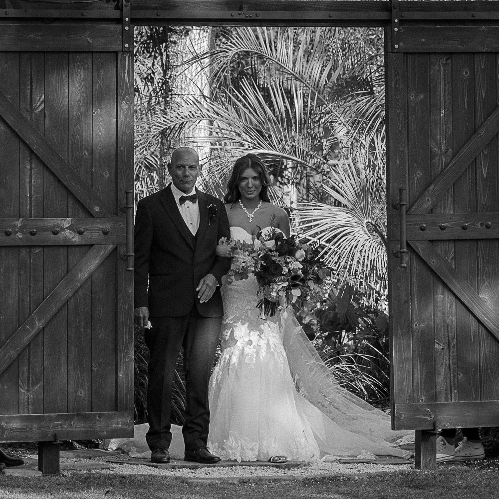 Bride and groom standing in a wooden doorway, with lush greenery behind them.