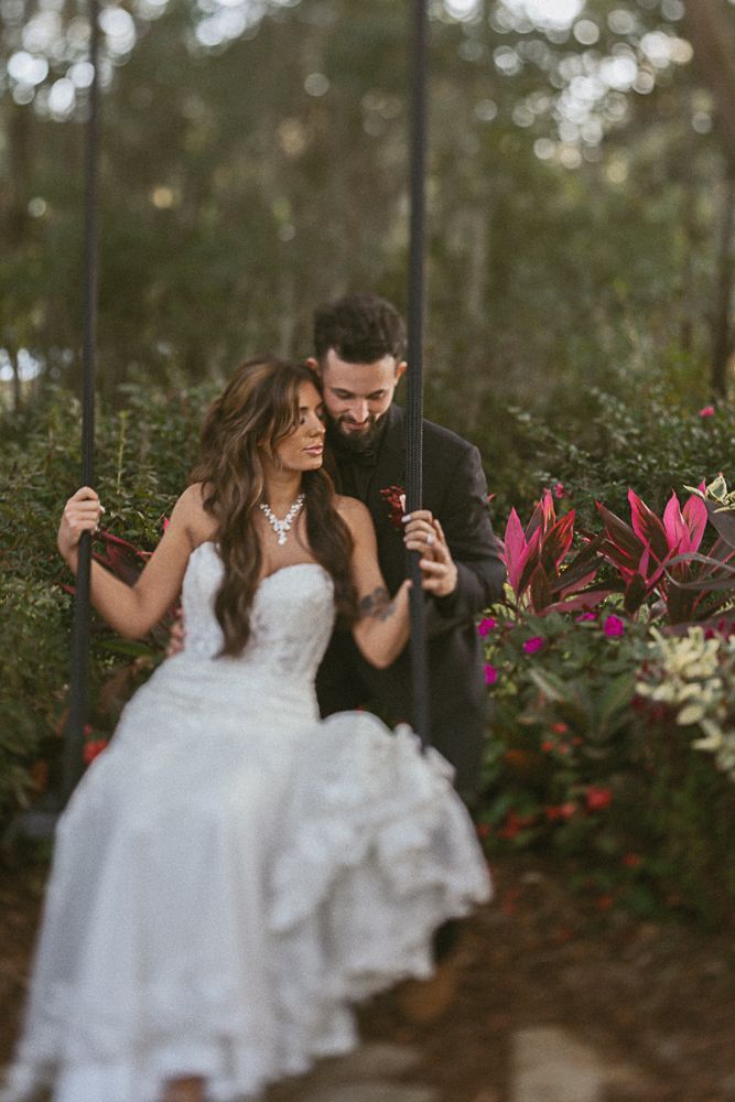 Bride and groom embracing in a garden, with white dress and dark suit amid pink flowers