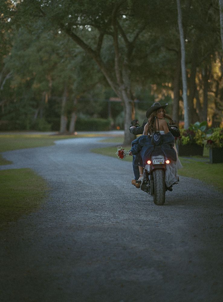 Motorcyclist riding away on a winding gravel road through a wooded park at dusk