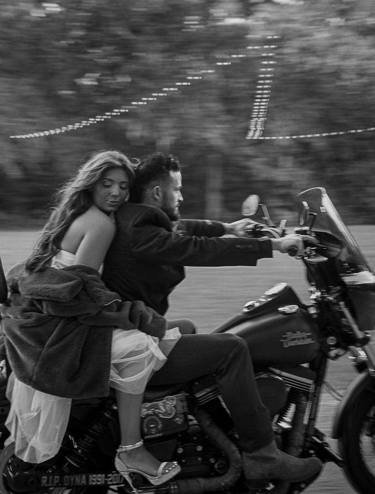Two people ride a motorcycle at night, with the passenger turning back and smiling.