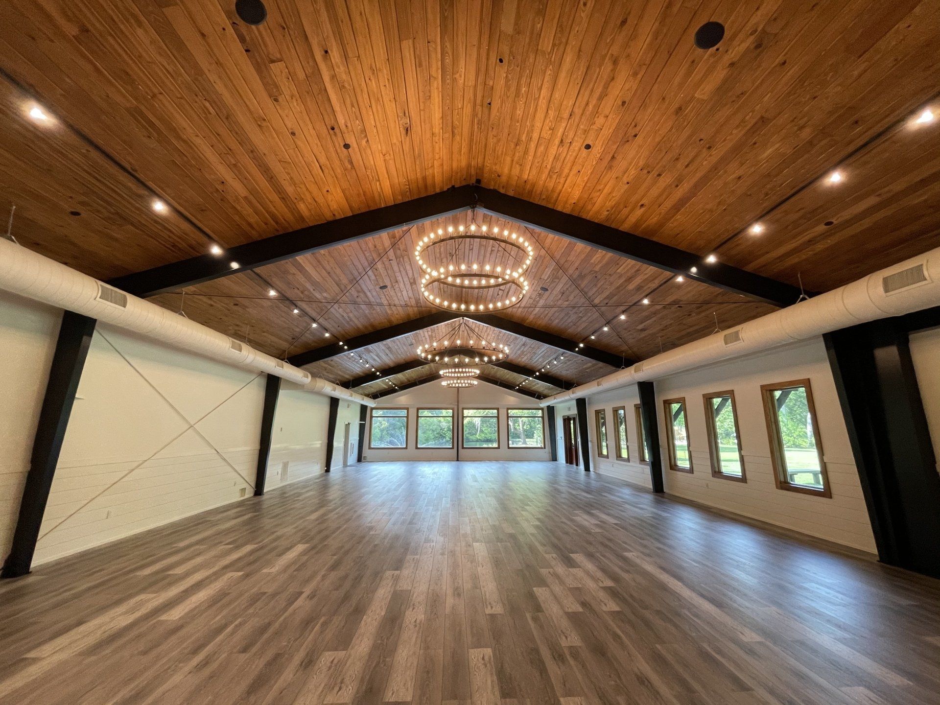 Empty banquet hall with wood-paneled ceiling, geometric chandeliers, and large windows.