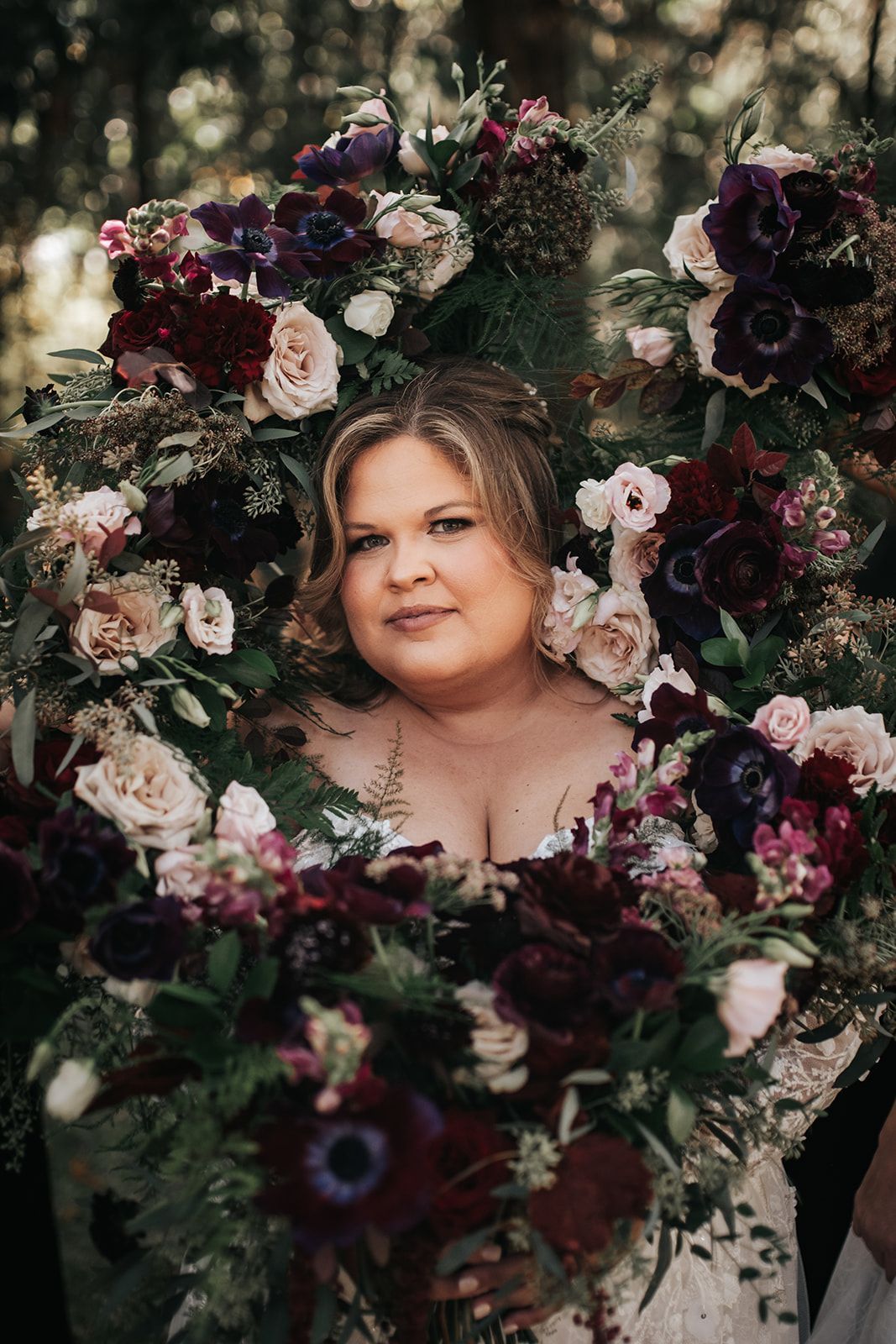 Woman framed by dark and white flowers, looking at the camera in a moody floral portrait