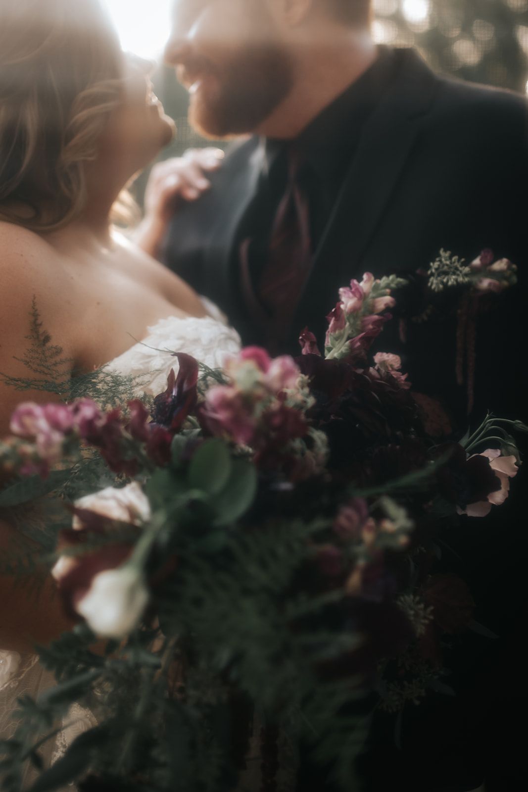 Couple in soft focus embracing, with a bouquet of pink and burgundy flowers in the foreground.