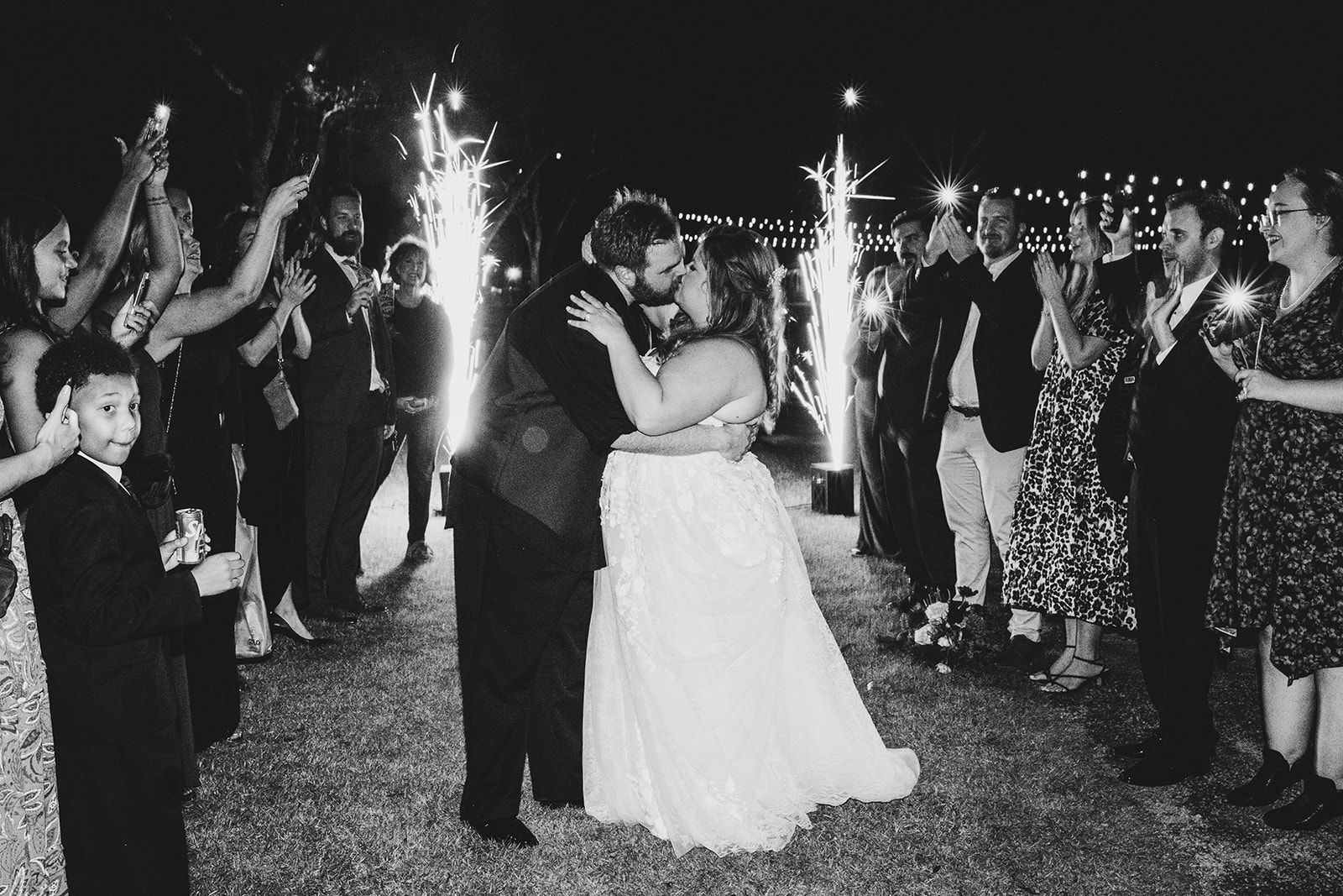 Bride and groom dancing amid sparklers at an outdoor celebration, guests applauding around them