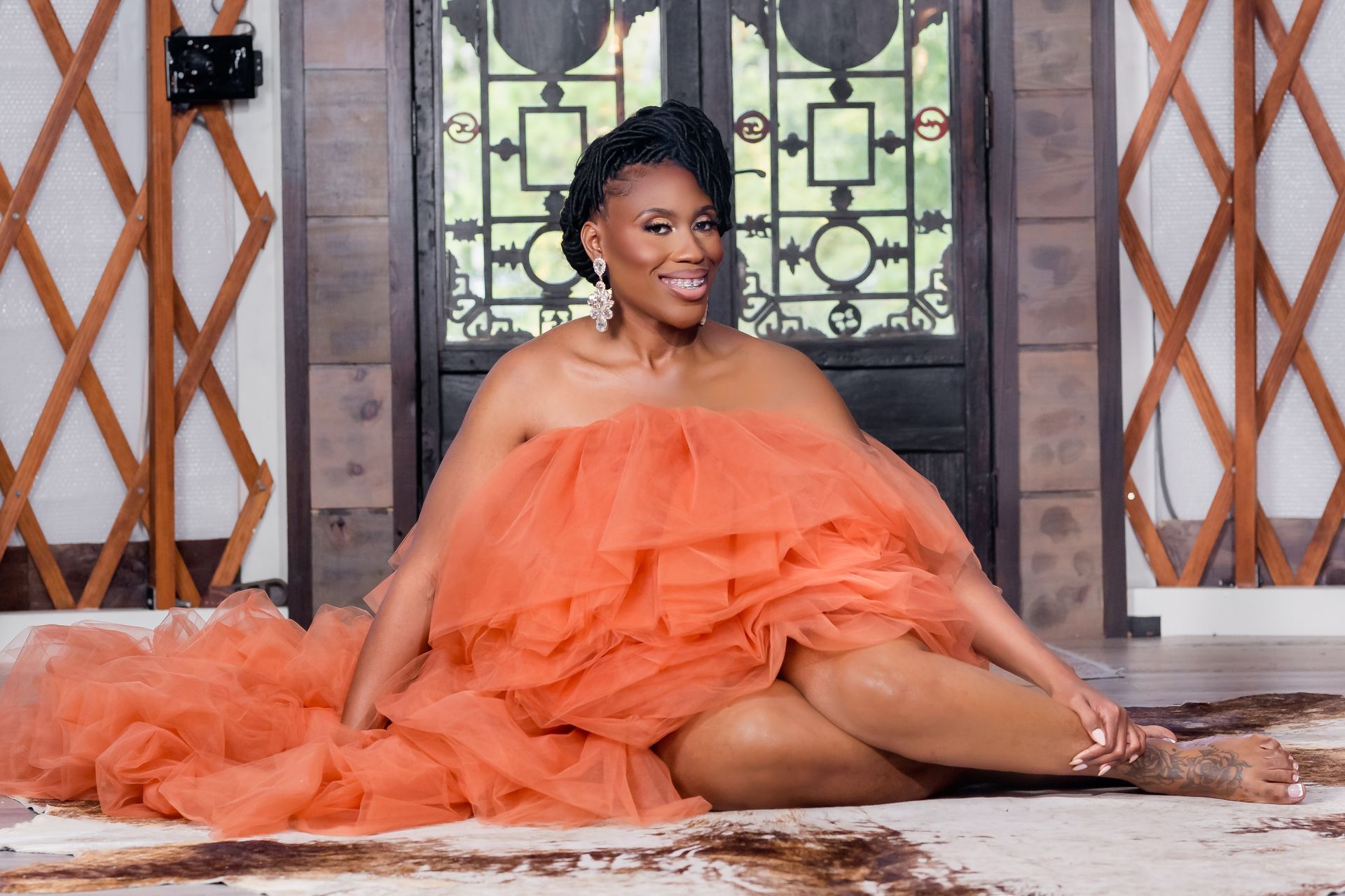 Woman in a voluminous orange gown sitting on steps in front of a decorative doorway.