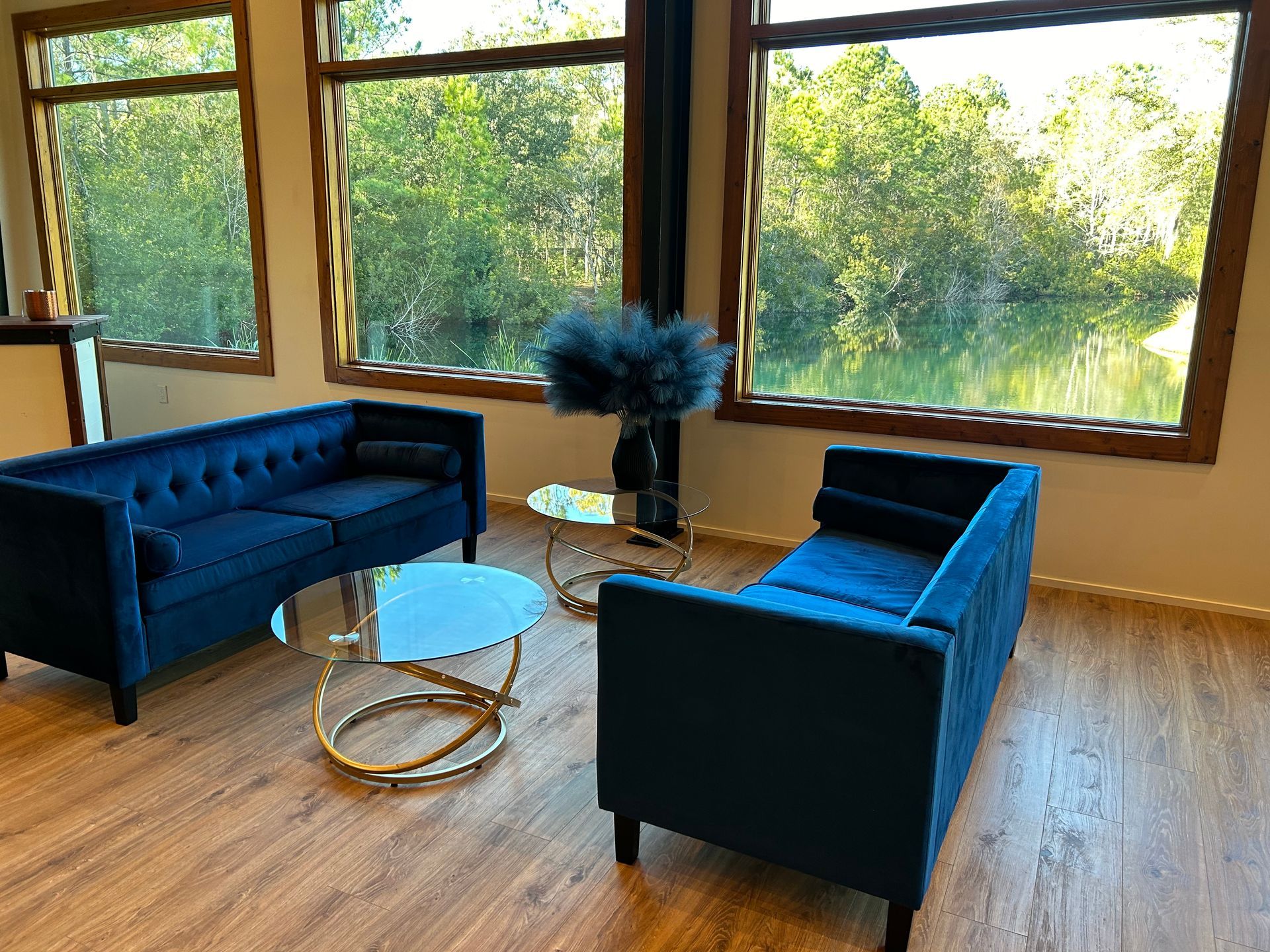 Blue velvet sofas in a bright living room with large windows, glass coffee table, and wood floor
