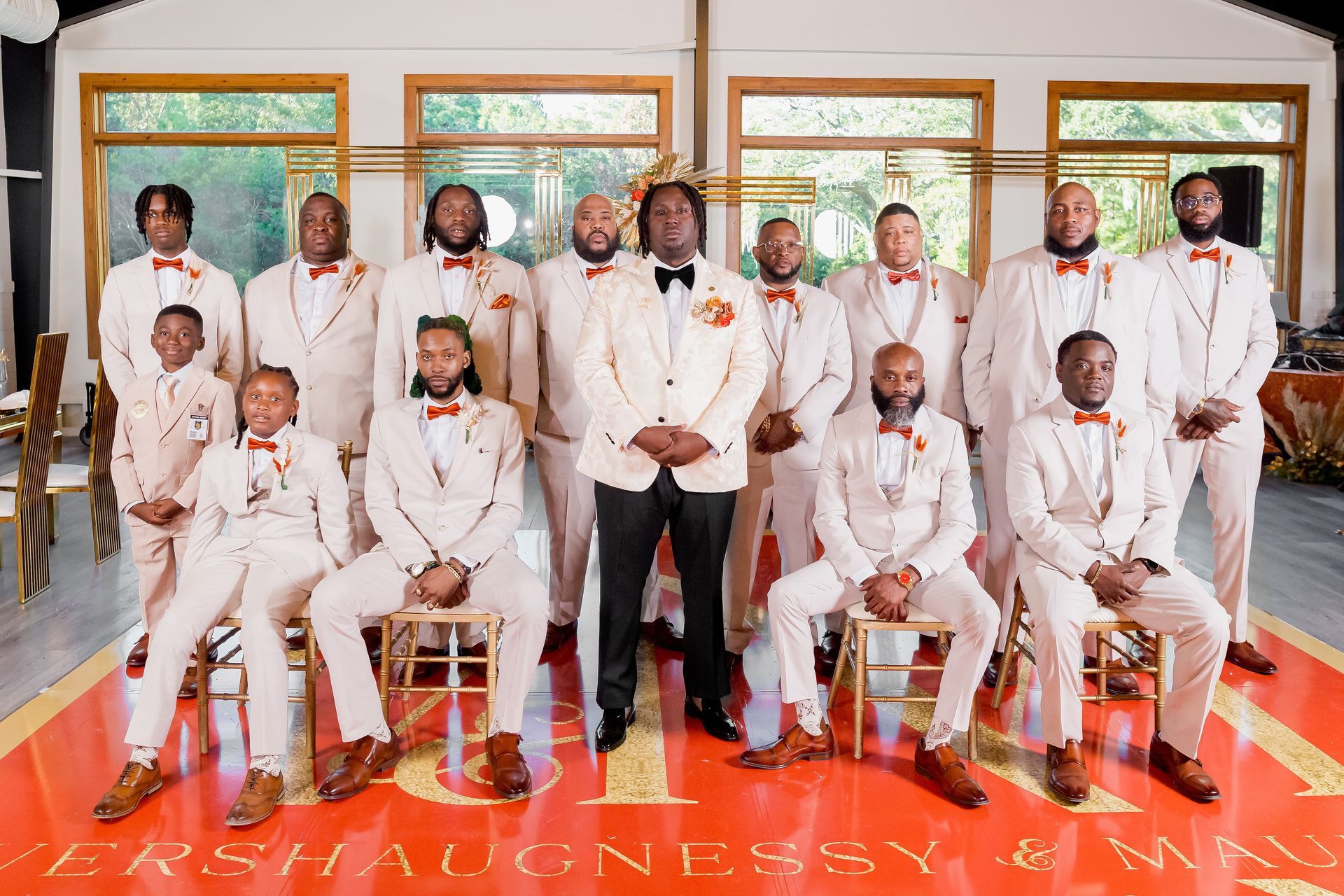 Group of people in white suits posing indoors on a red carpet in front of large windows