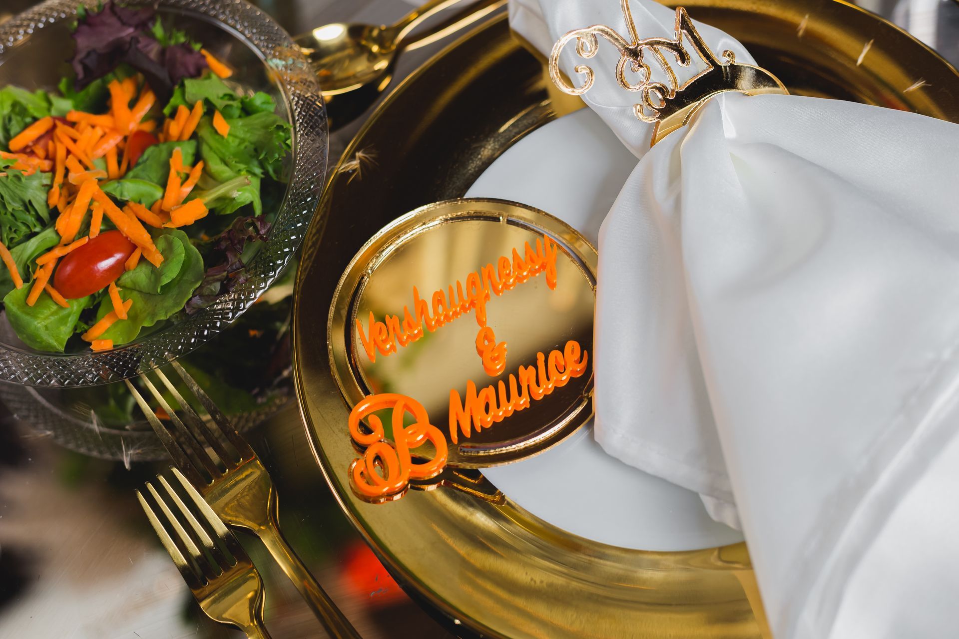 Elegant gold table setting with white napkin, salad, and a gold name card reading “DB M…”